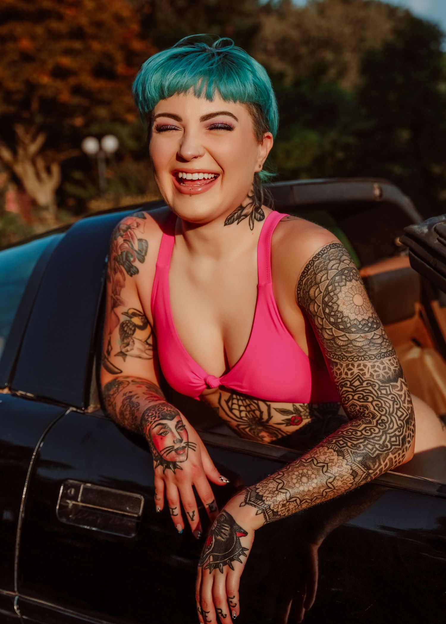 Boudoir portrait of beautiful blue hair tattooed woman in pink laughing with vintage car for photoshoot with Boudoir by Bri in Saint Louis