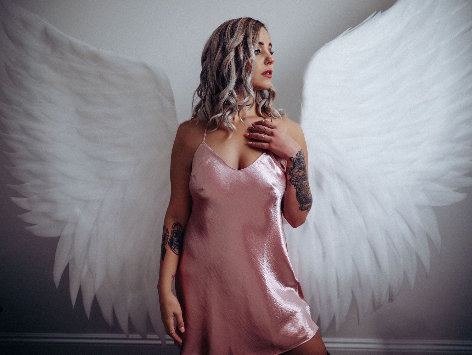 Boudoir portrait of beautiful young tattooed woman posing in huge white angel wings and pink nightie for photoshoot with Boudoir by Bri