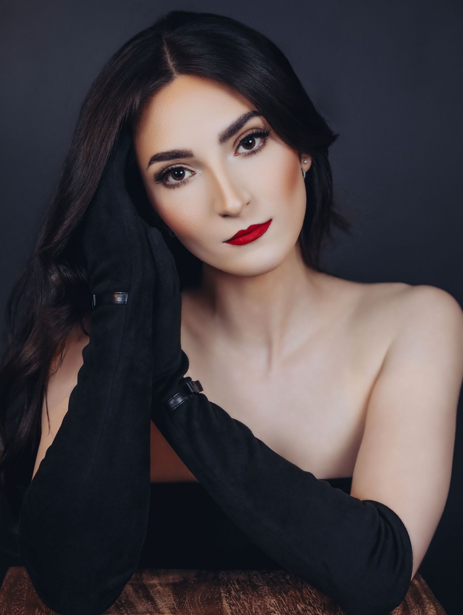Formal portrait of pale woman with long, black hair, professional glam makeup with red lipstick, wearing black velvet elbow-length gloves.