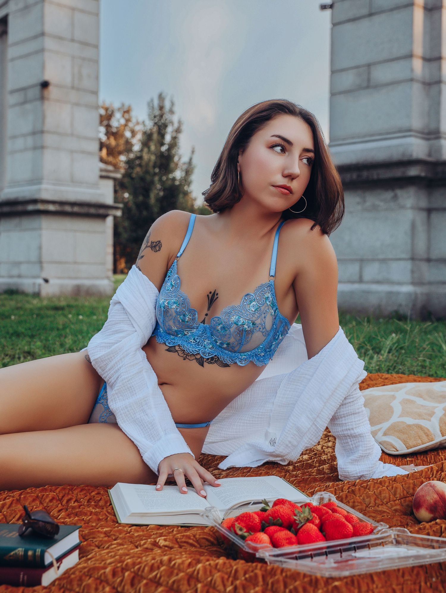 Beautiful young woman in blue lingerie tattoos reading in park with strawberries at picnic for session with Boudoir by Bri Saint Louis