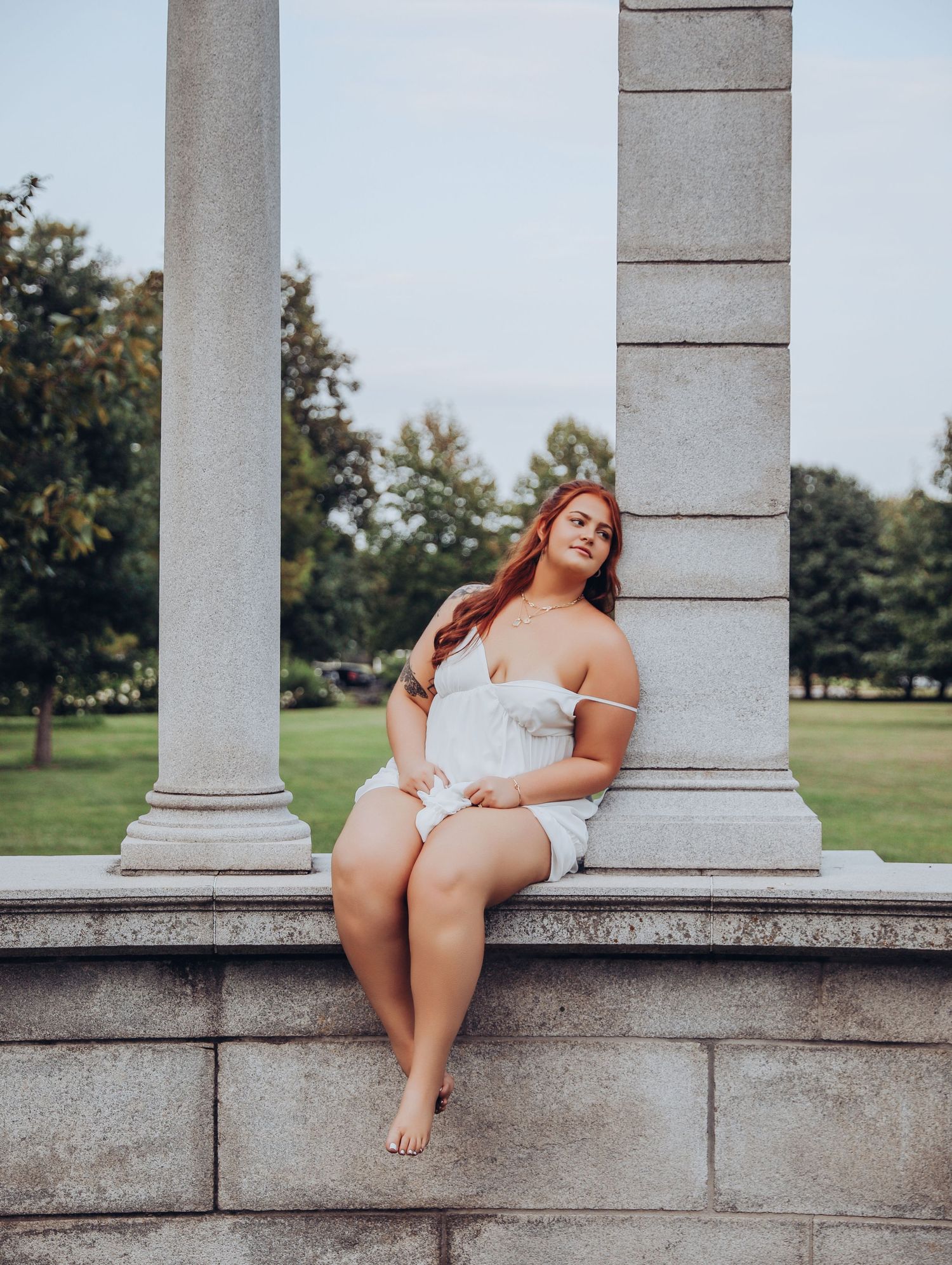 Beautiful young woman posing by marble pillars in white dress draping off shoulders for photoshoot Boudoir by Bri Saint Louis Forest Park