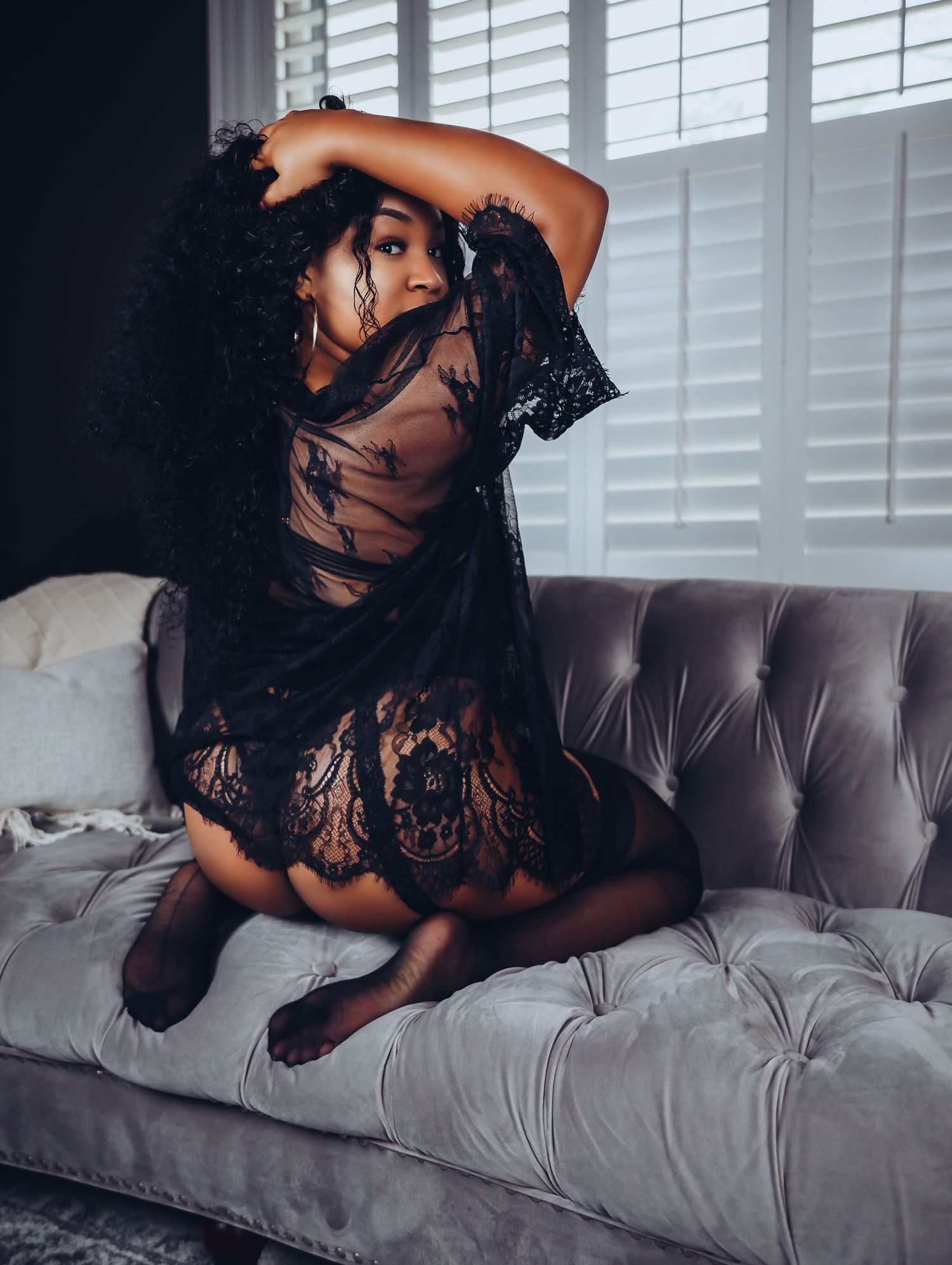 Beautiful woman kneeling on vintage couch in bedroom looking over shoulder in black lingerie set and stockings Boudoir by Bri in Saint Louis