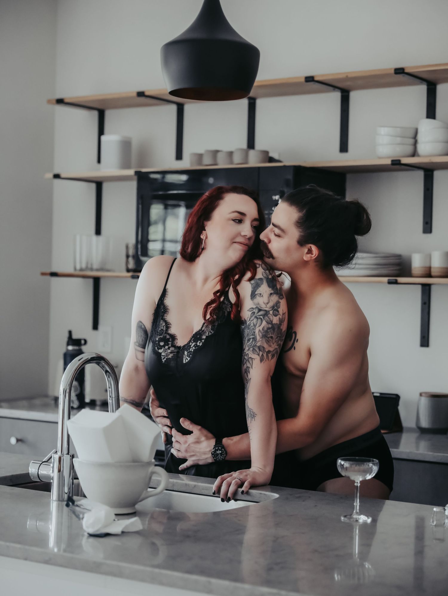 Boudoir portrait of young alternative couple in love flirting in kitchen while cooking for photoshoot with Boudoir by Bri in Saint Louis