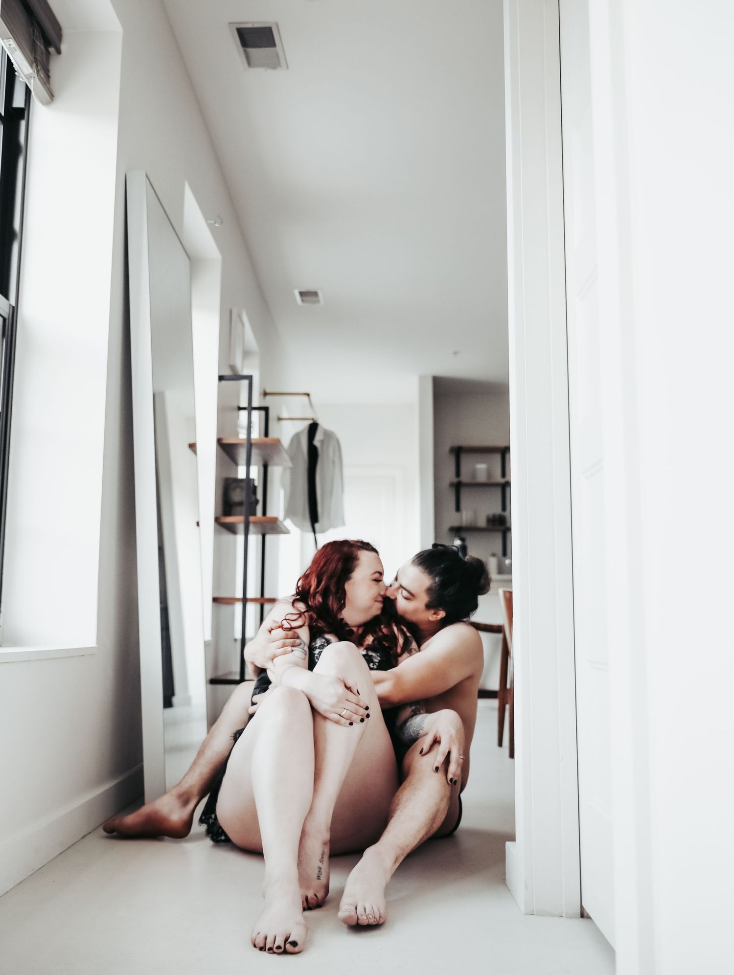 Boudoir portrait of flirty young couple in love holding each other close in white hallway for photoshoot with Boudoir by Bri Saint Louis