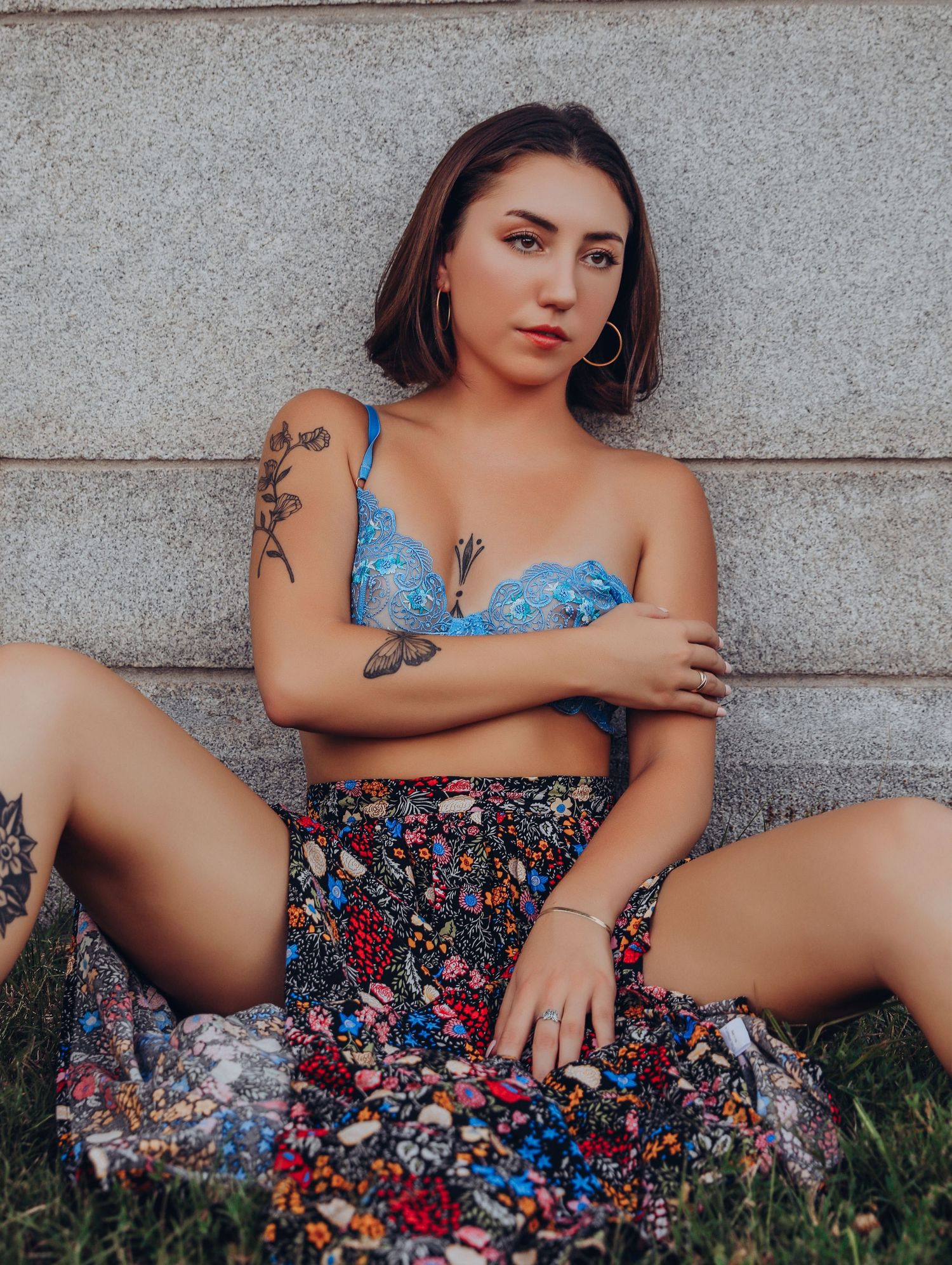 Young woman in blue bra and floral maxi skirt posing on grass leaning against marble wall with short hair and tattoos for Boudoir by Bri STL