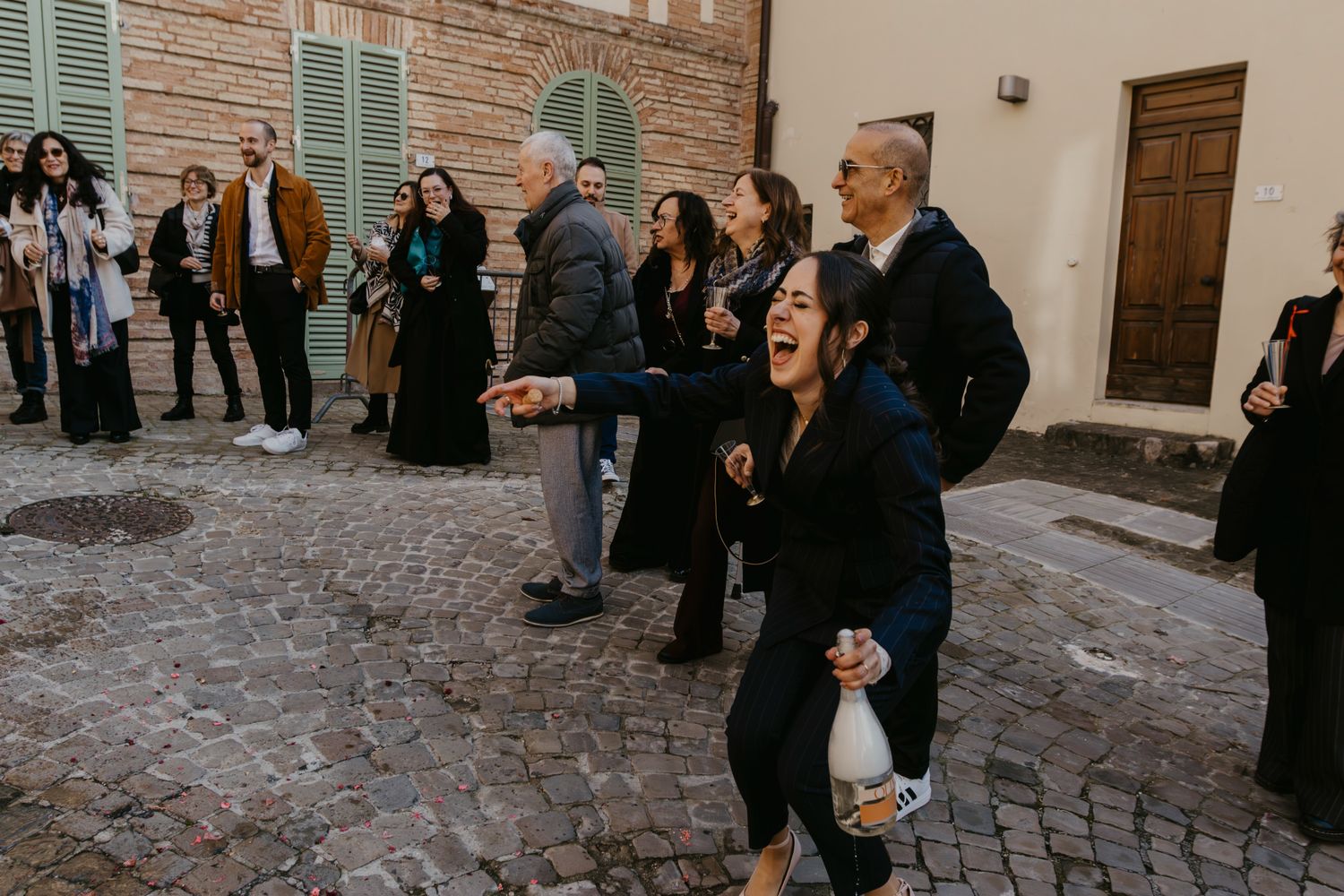 A group of joyful guests laughing and celebrating outdoors in a rustic Italian courtyard during a wedding