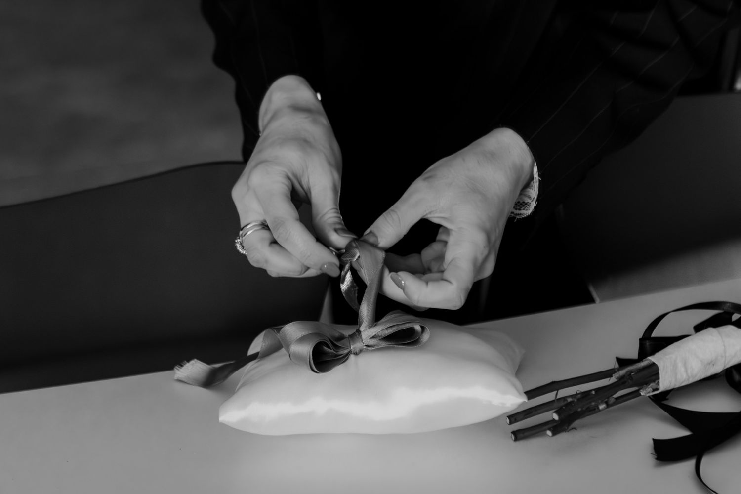 Hands sewing ribbons onto a ballet pointe shoe on a white table in black and white.