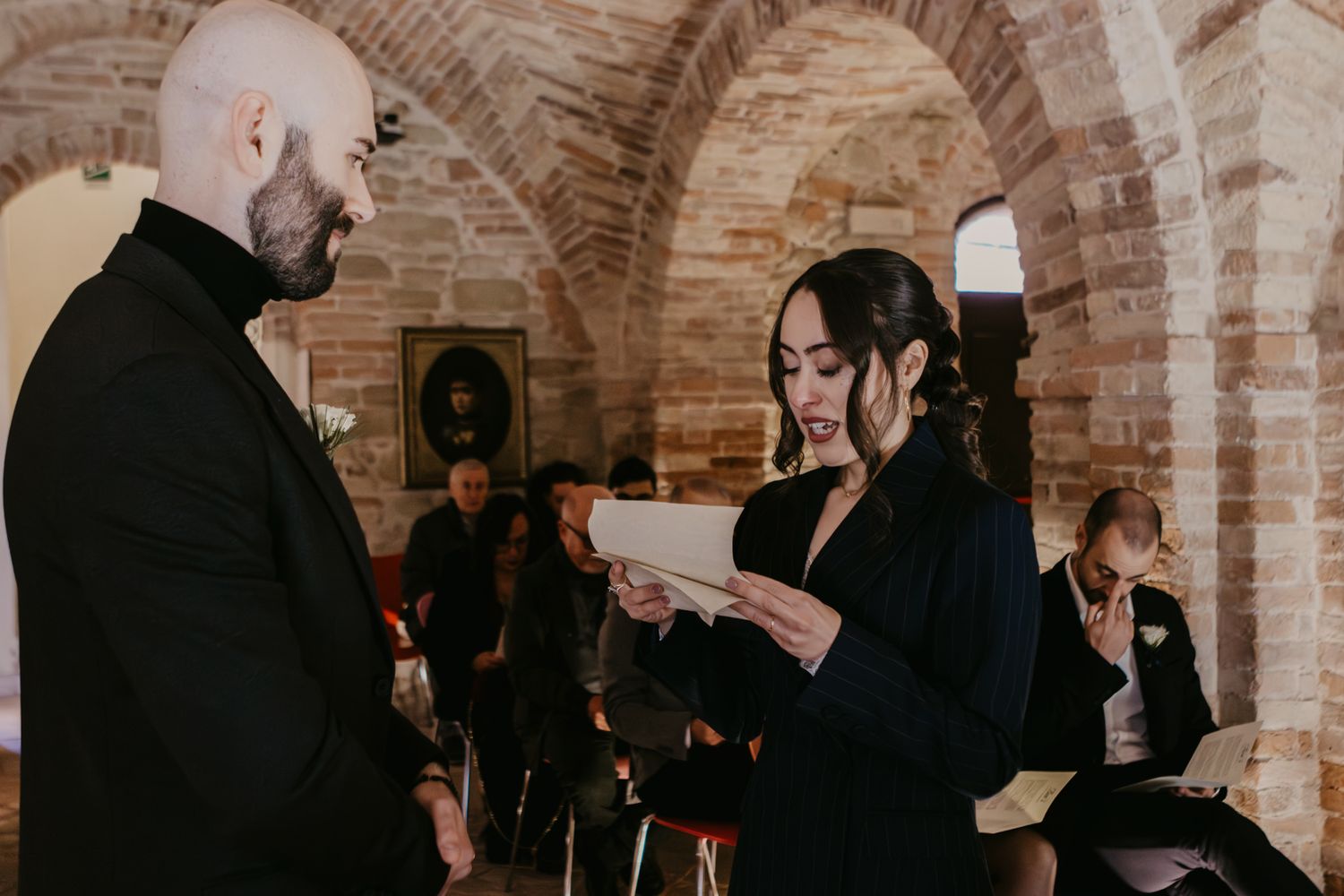 Bride reads vows to groom in rustic brick chapel during intimate wedding ceremony.