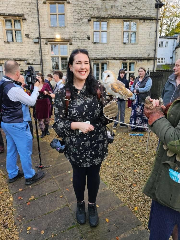 Woman smiling while holding a barn owl on a gloved hand outdoors at a historic stone building event.