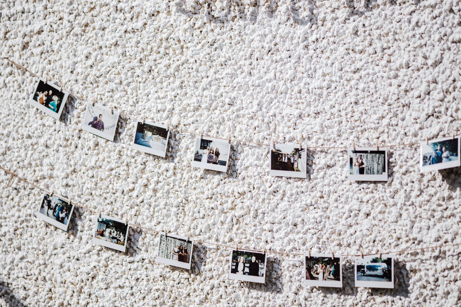 Polaroid photos displayed on string lights against a white textured wall, creating a charming photo gallery display.
