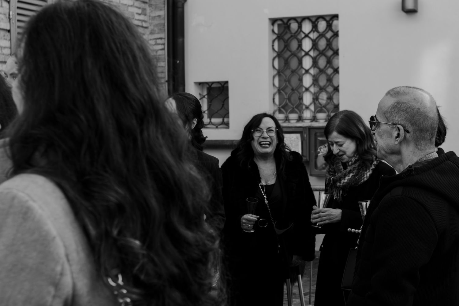 Black and white photo of a group of people socializing and laughing at a wedding.