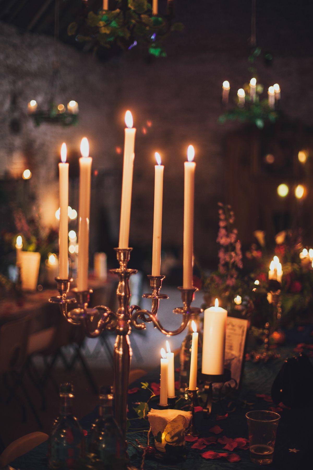 Elegant candlelit event decor with brass candelabra and glowing tapered candles in a warmly lit rustic venue.