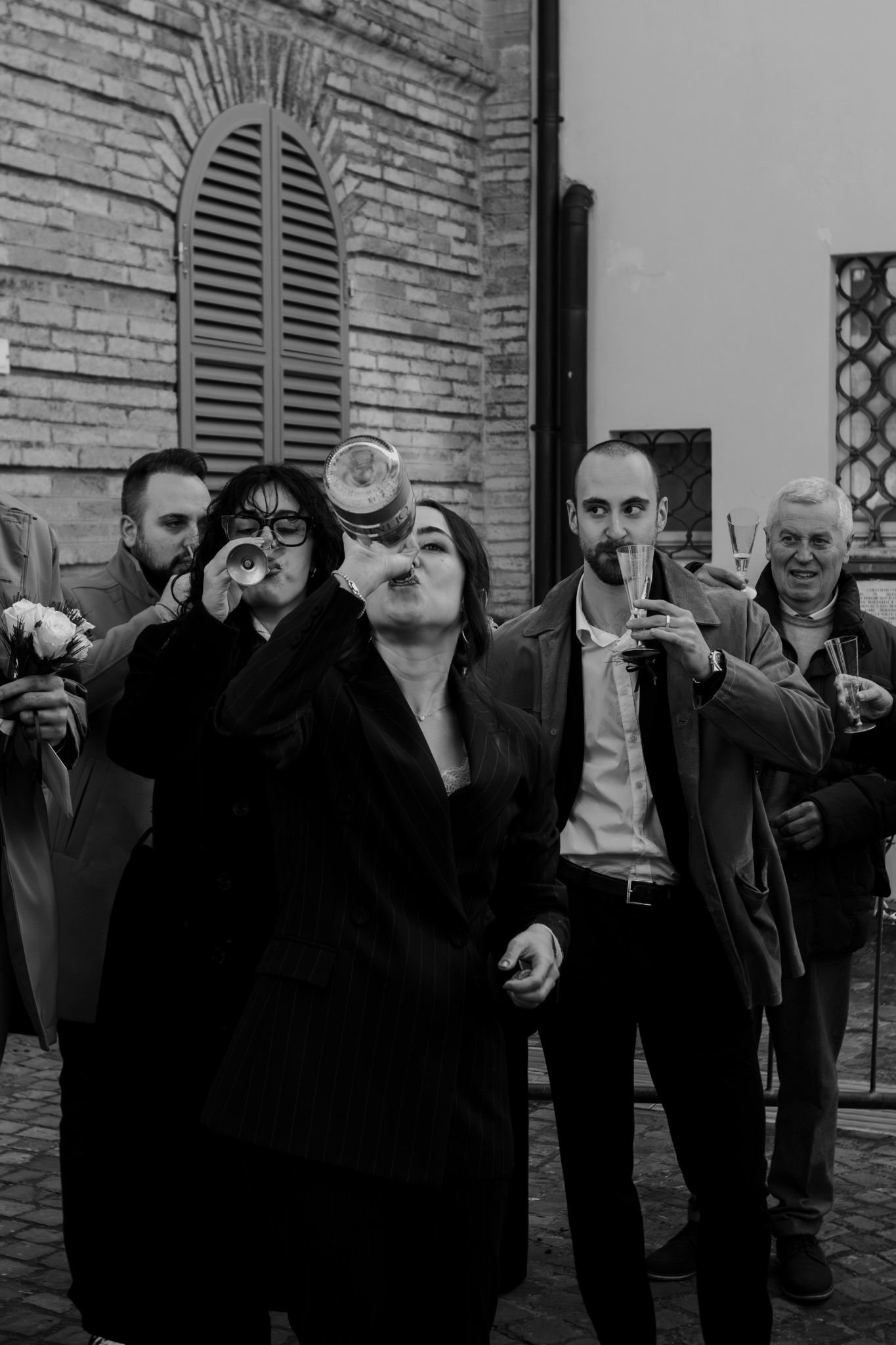 Black and white photo of guests drinking champagne and celebrating outdoors at a wedding reception.