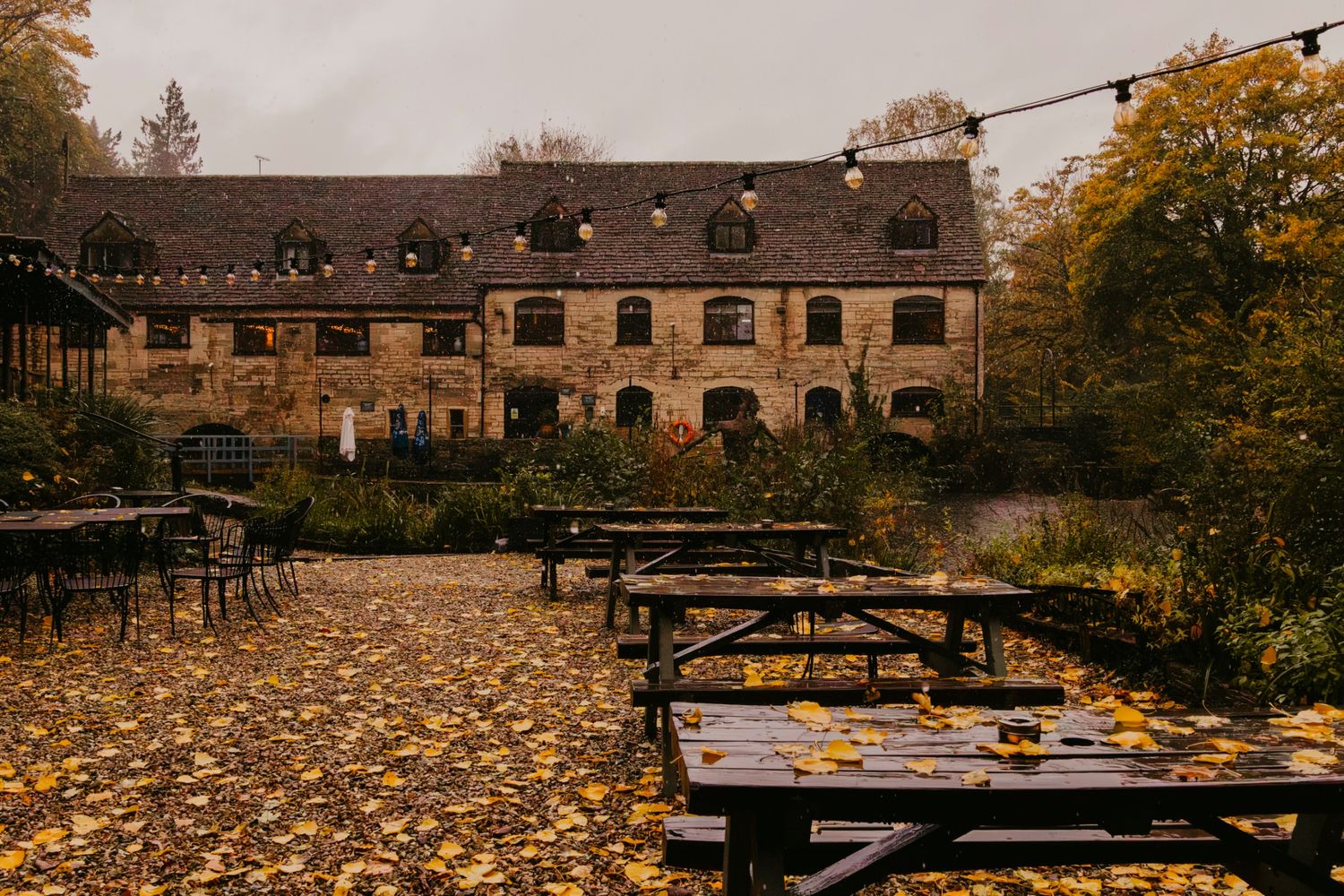 Autumn outdoor seating area at Egypt Mill with wooden picnic tables covered in fallen leaves