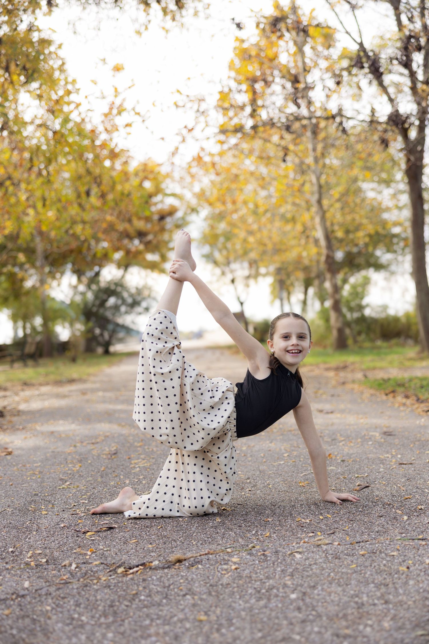 A series of four action shots showing a child in a polka dot dress performing dance poses on a path in autumn.