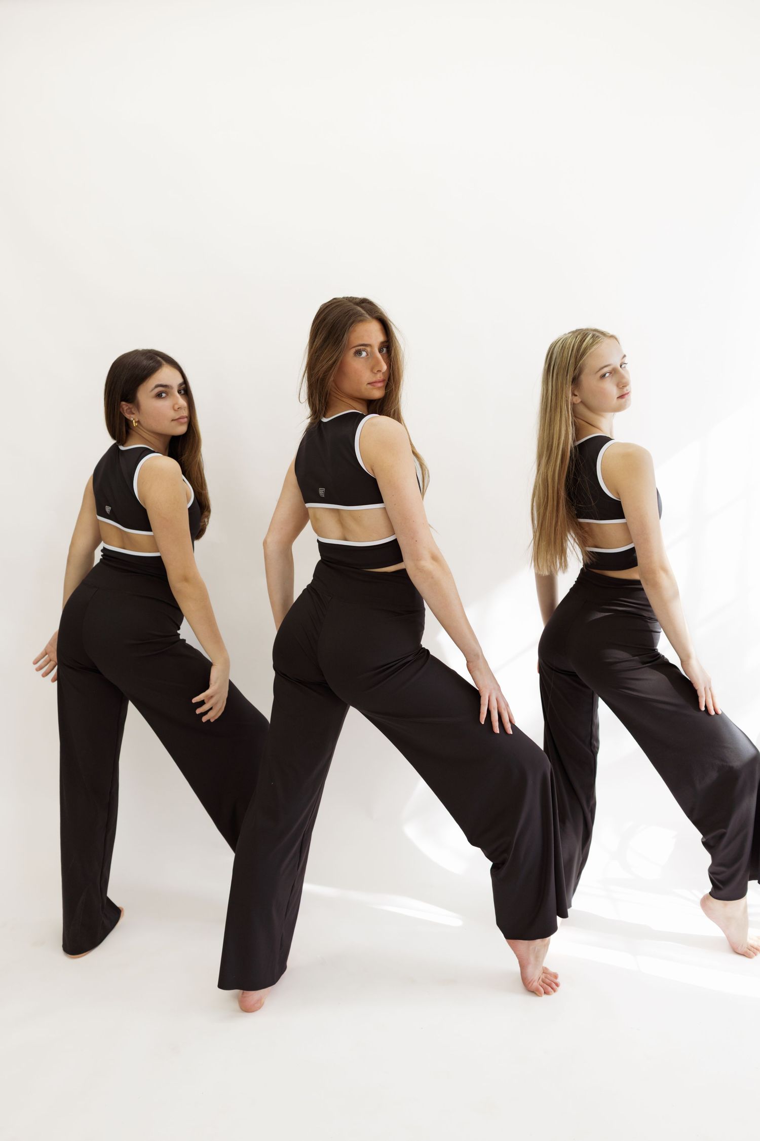 Three dancers in matching black and white attire pose with their backs to camera.