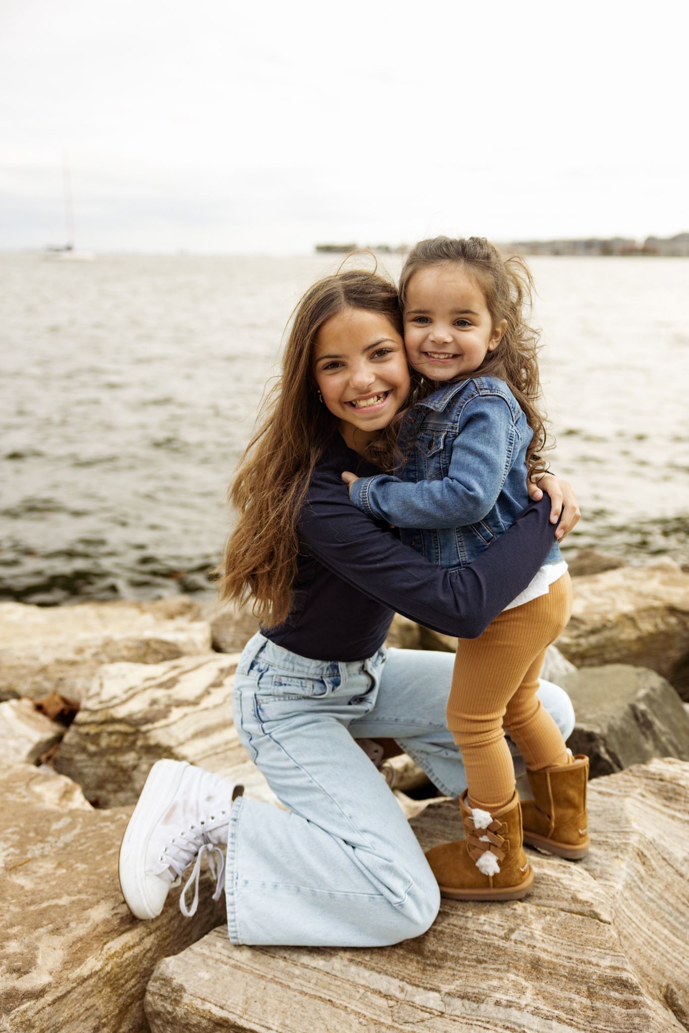 Two people embrace while sitting on coastal rocks near the water.