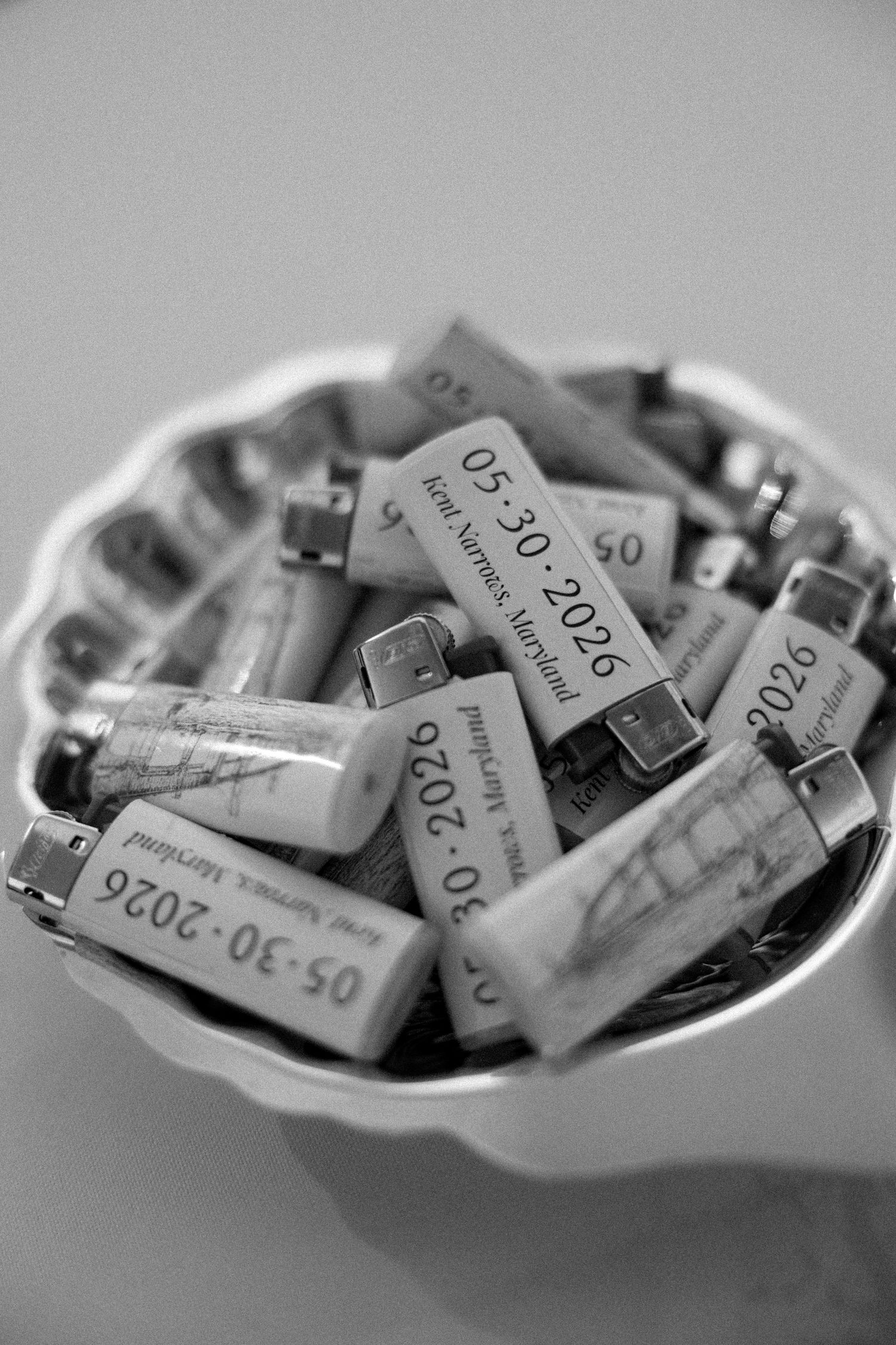 Black and white photo of personalized lighters in a decorative bowl, engraved with 05-30-2026 and Anne Arundel, Maryland.