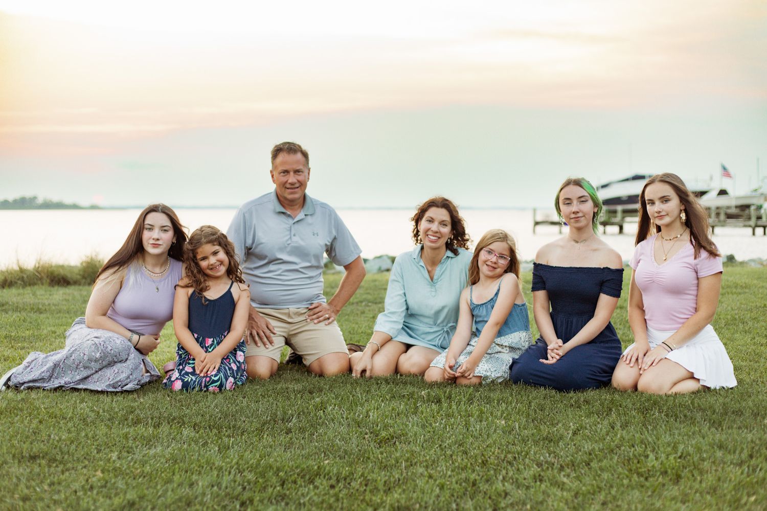 Happy family sitting together on grass at sunset near the beach.