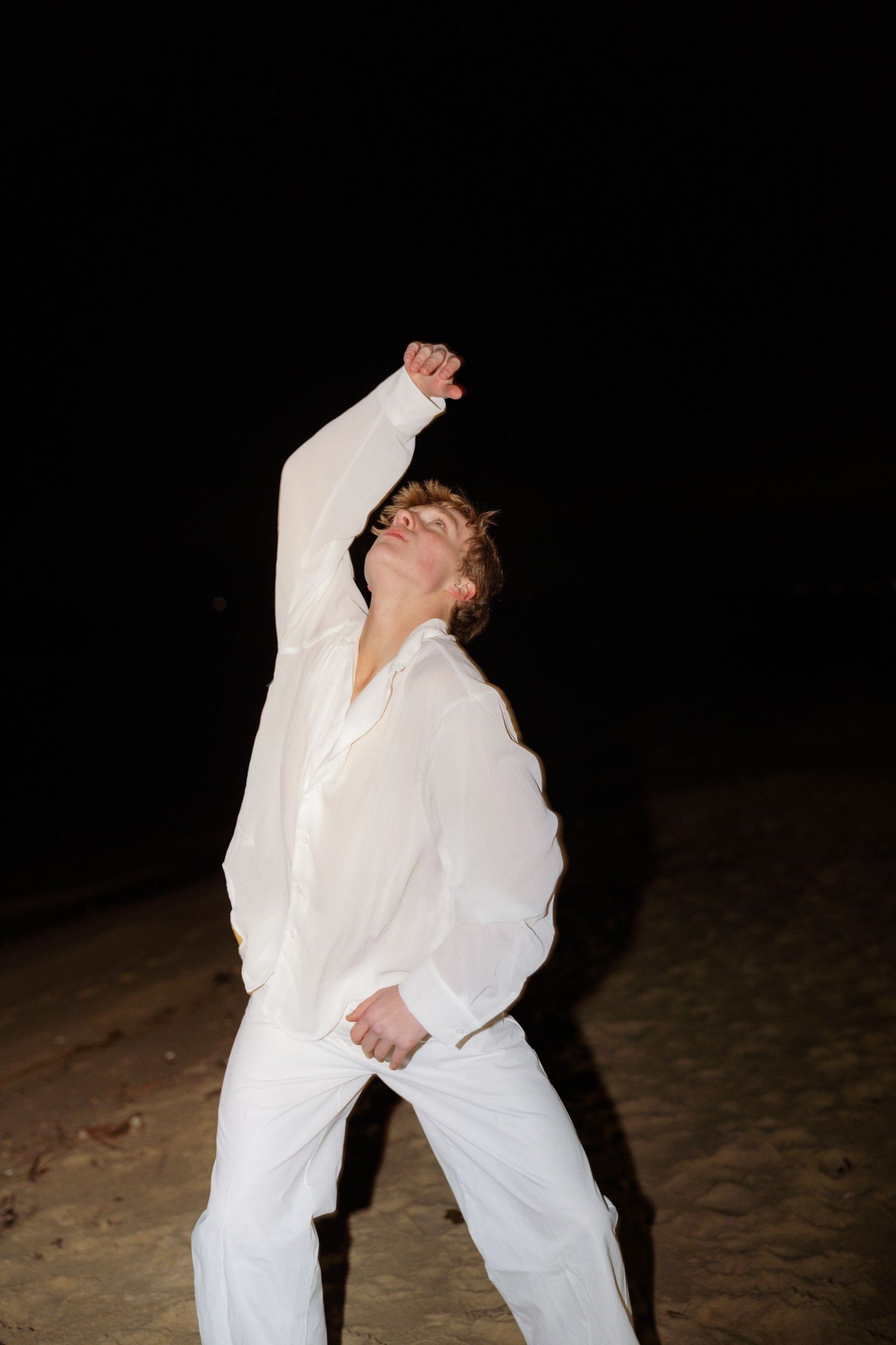 Person in all-white outfit dancing energetically at night on a dark background.