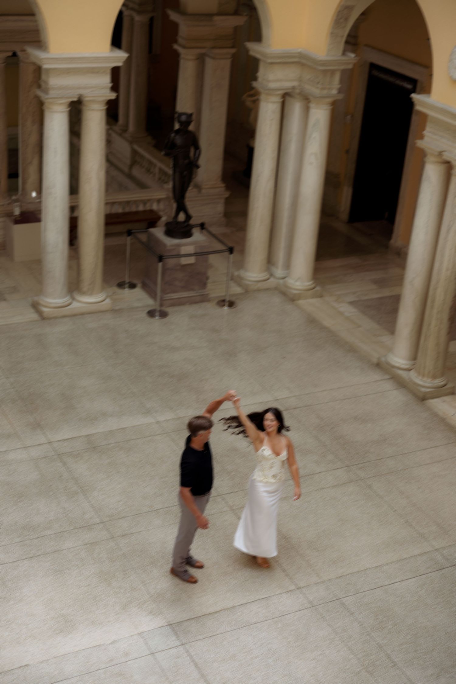 A couple performs a romantic dance sequence in a grand hall with ornate white columns and marble floors.