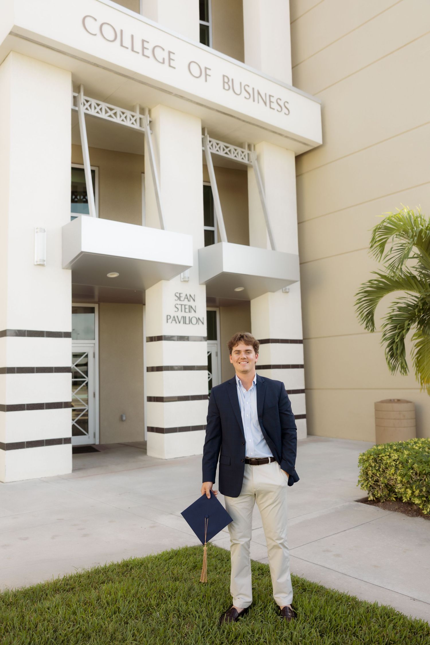 Graduate stands outside College of Business building holding diploma.