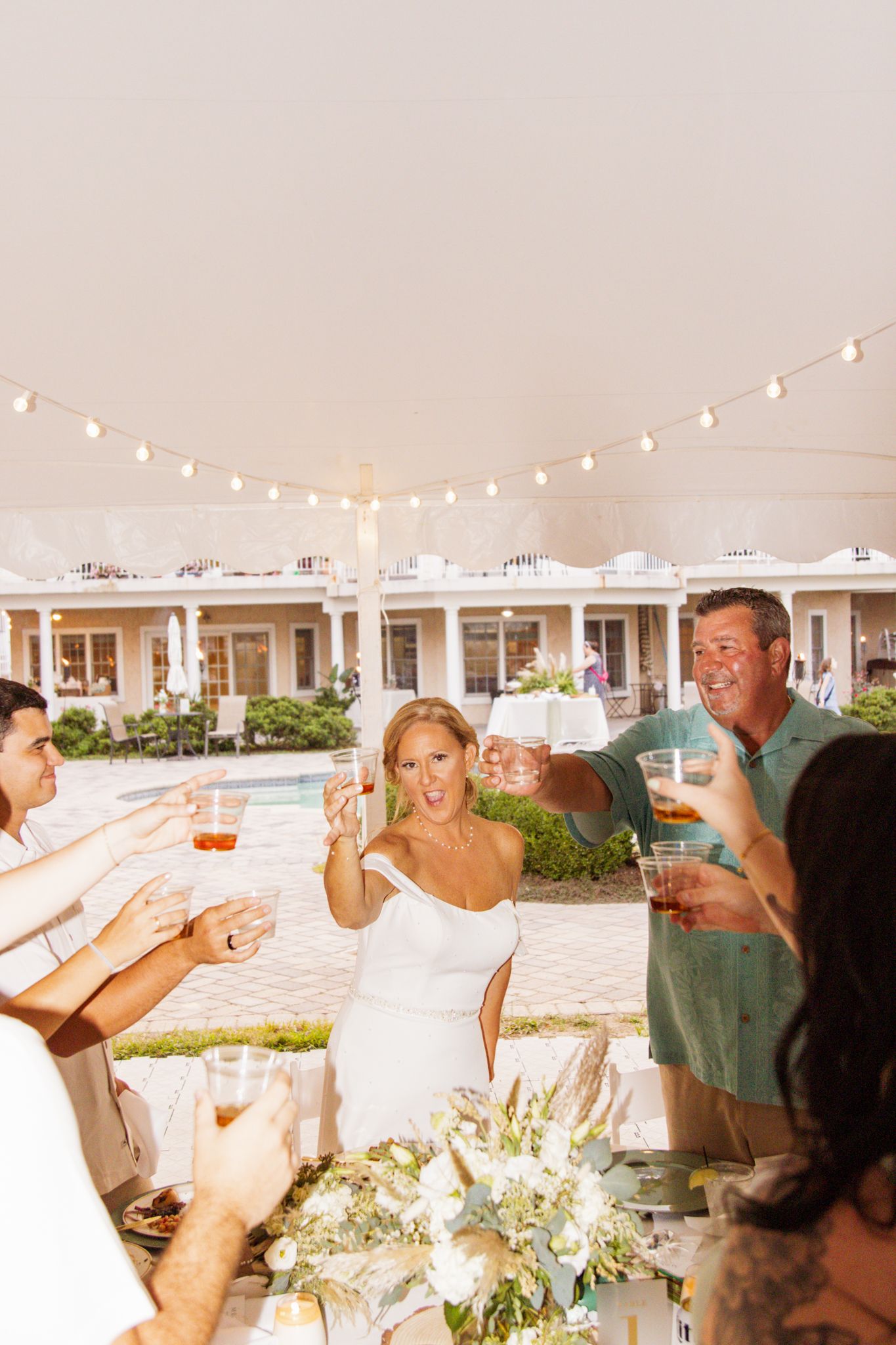 Wedding celebration on outdoor patio with string lights as guests raise glasses in a toast.