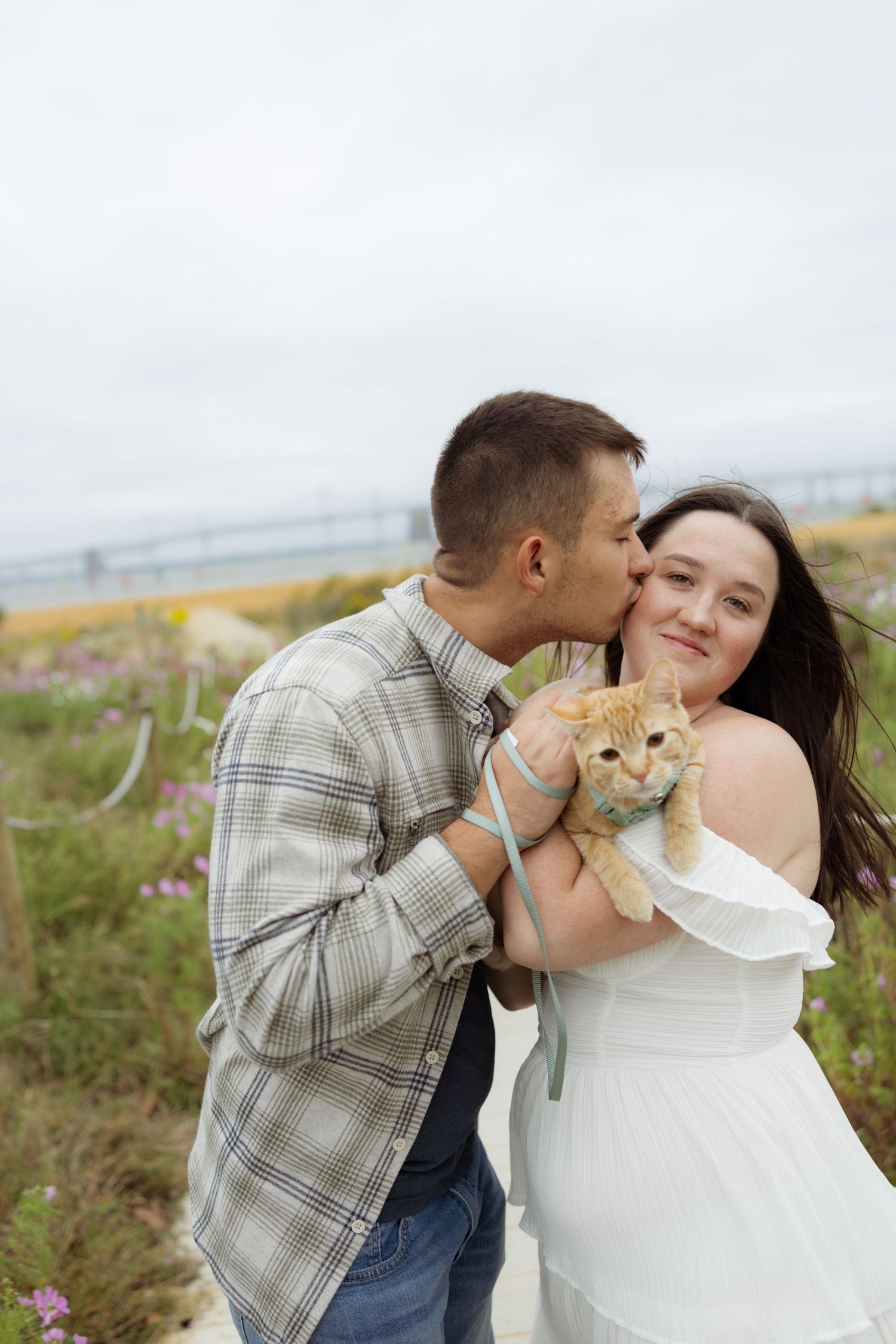 A couple shares romantic moments in a grassy field with wildflowers on a cloudy day.