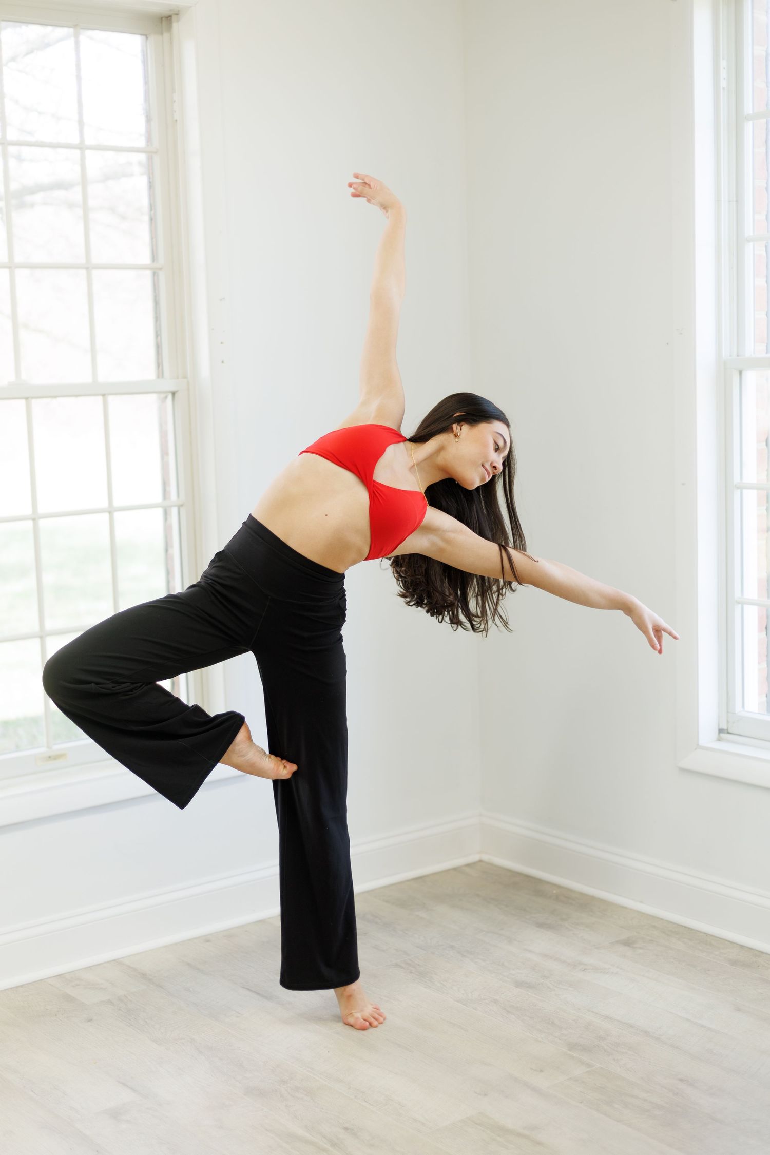 Dancer in red crop top and black pants performs graceful movement in bright studio space.