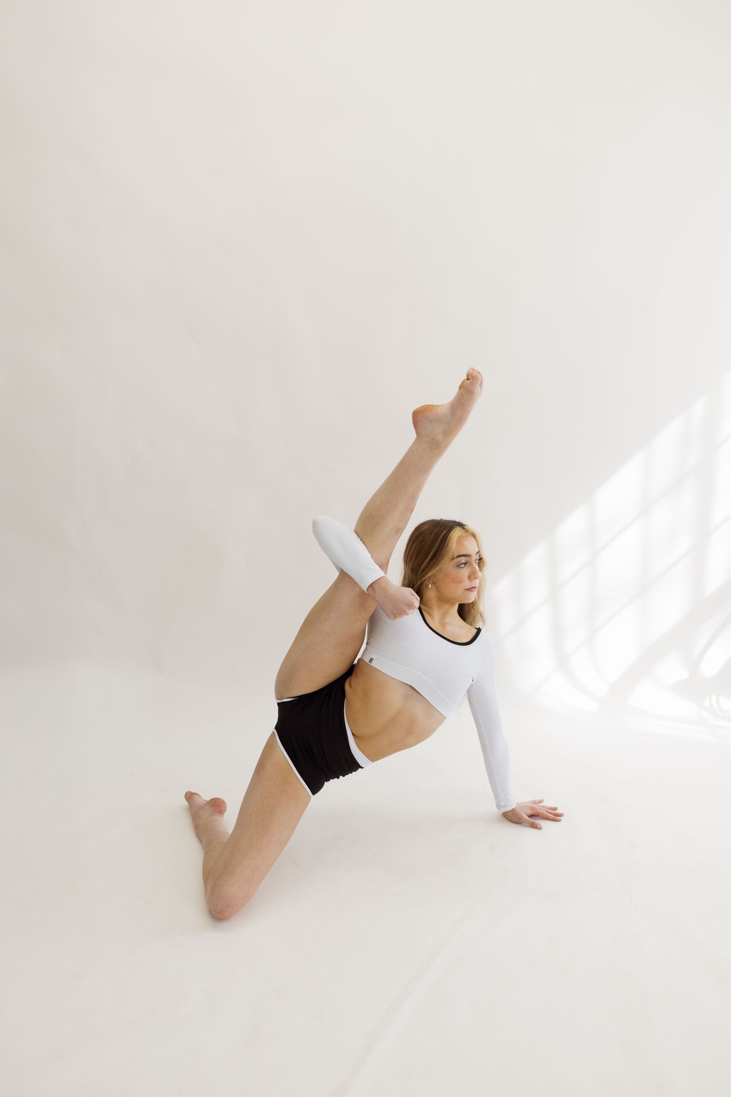 Dancer in white and black attire performs floor movement in bright studio setting.