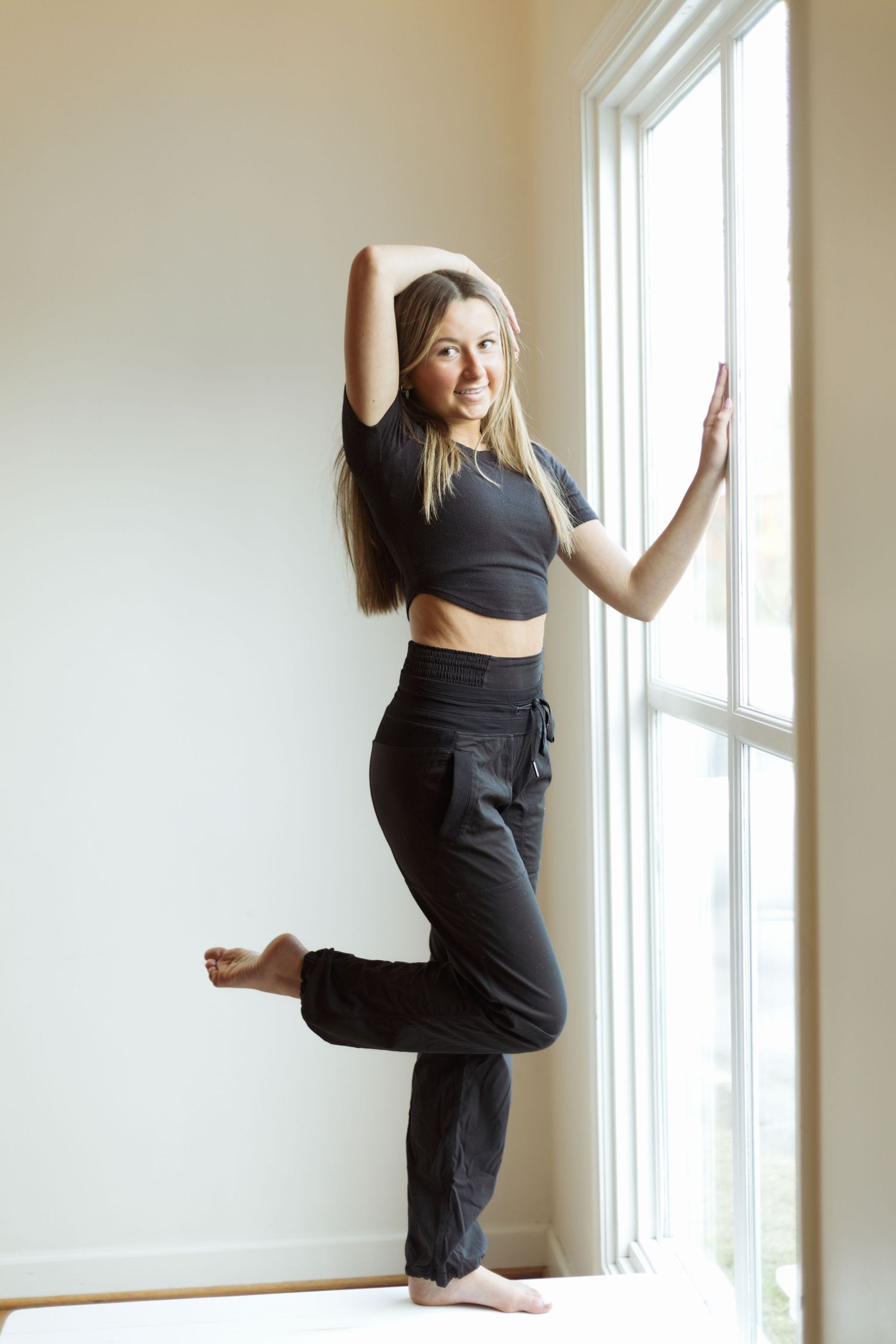 Dancer in crop top and pants poses gracefully by bright window.