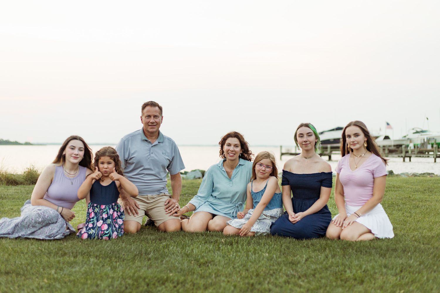 Family group sitting together on grassy lawn by waterfront at sunset.