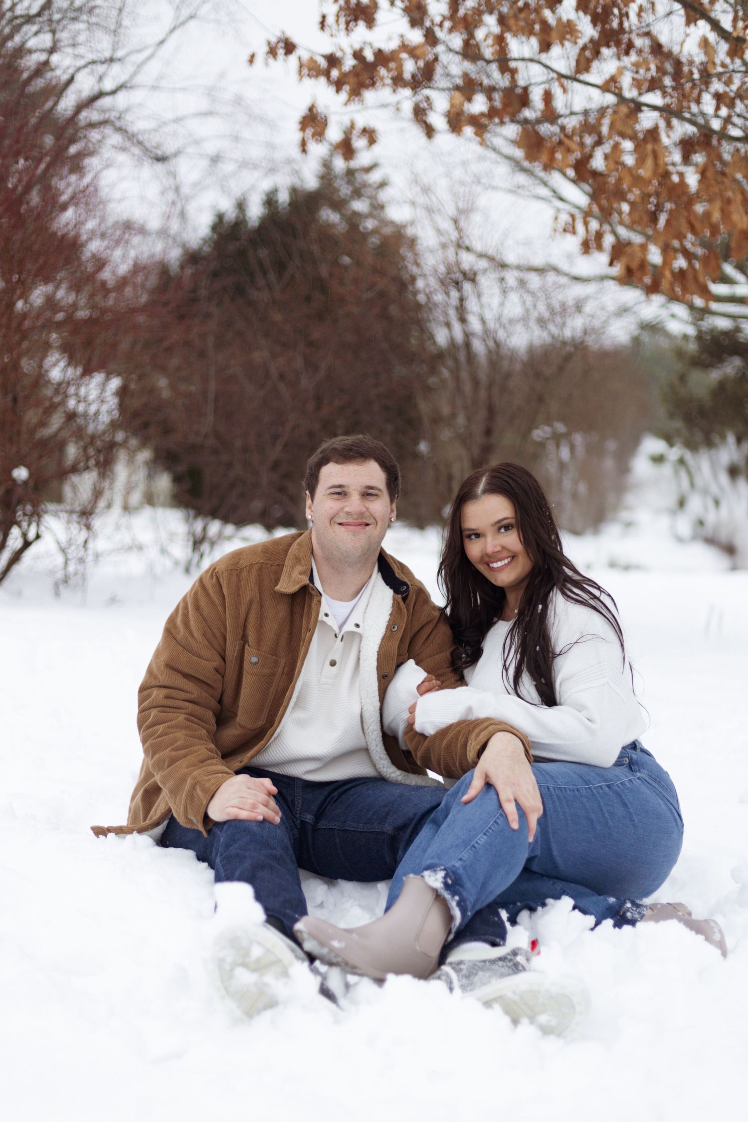 Happy couple sitting together in fresh snow during winter photoshoot.