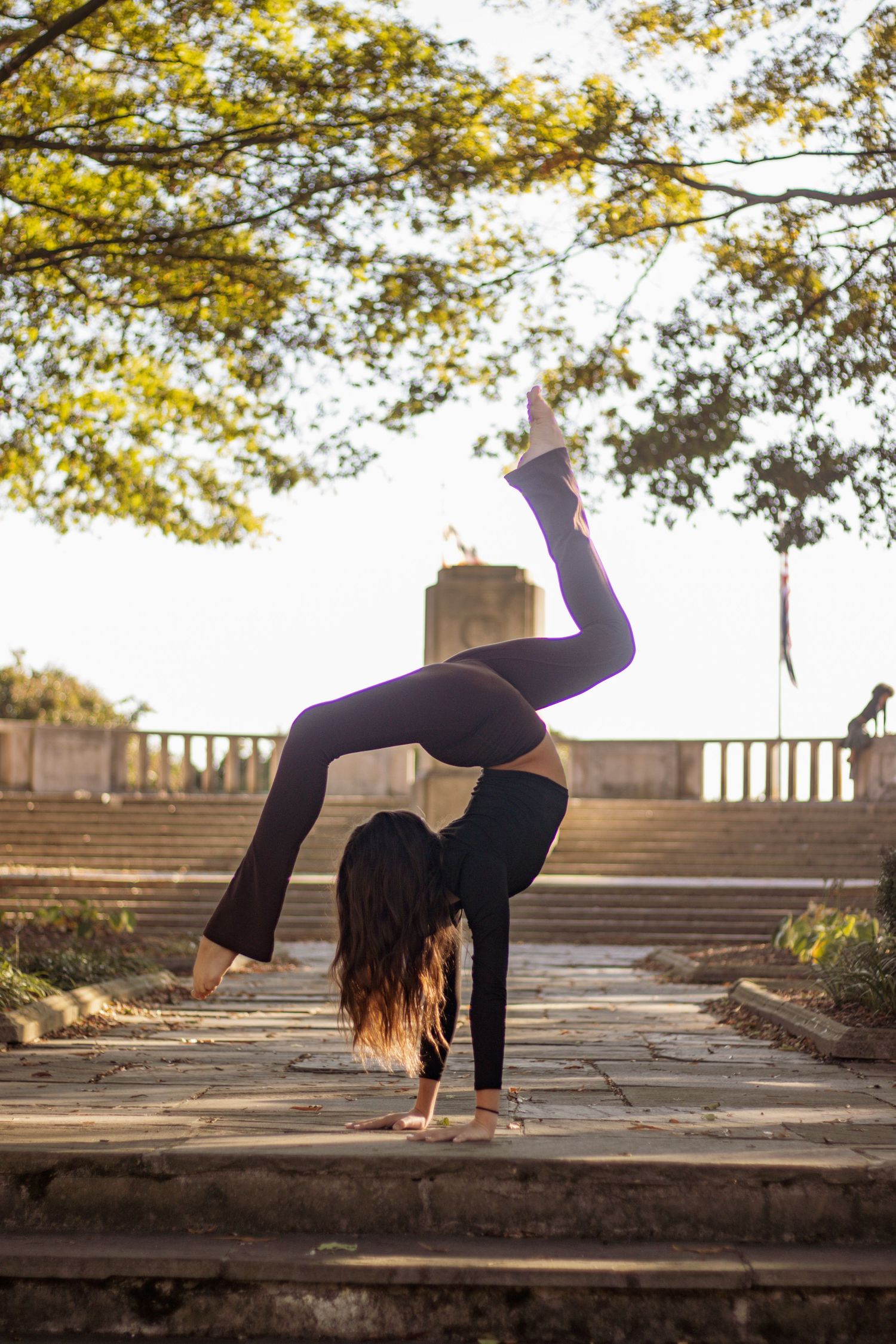 Silhouetted dancer performs handstand on stone steps under autumn trees.