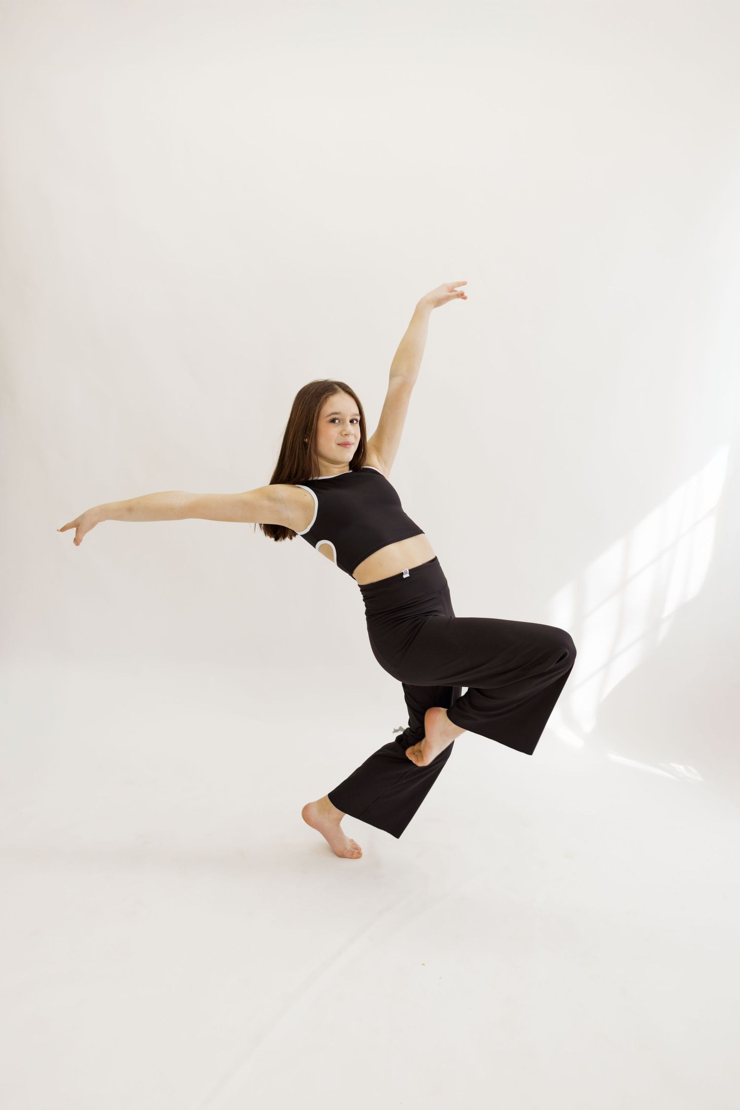Modern dancer in black attire strikes dynamic pose against white studio background.