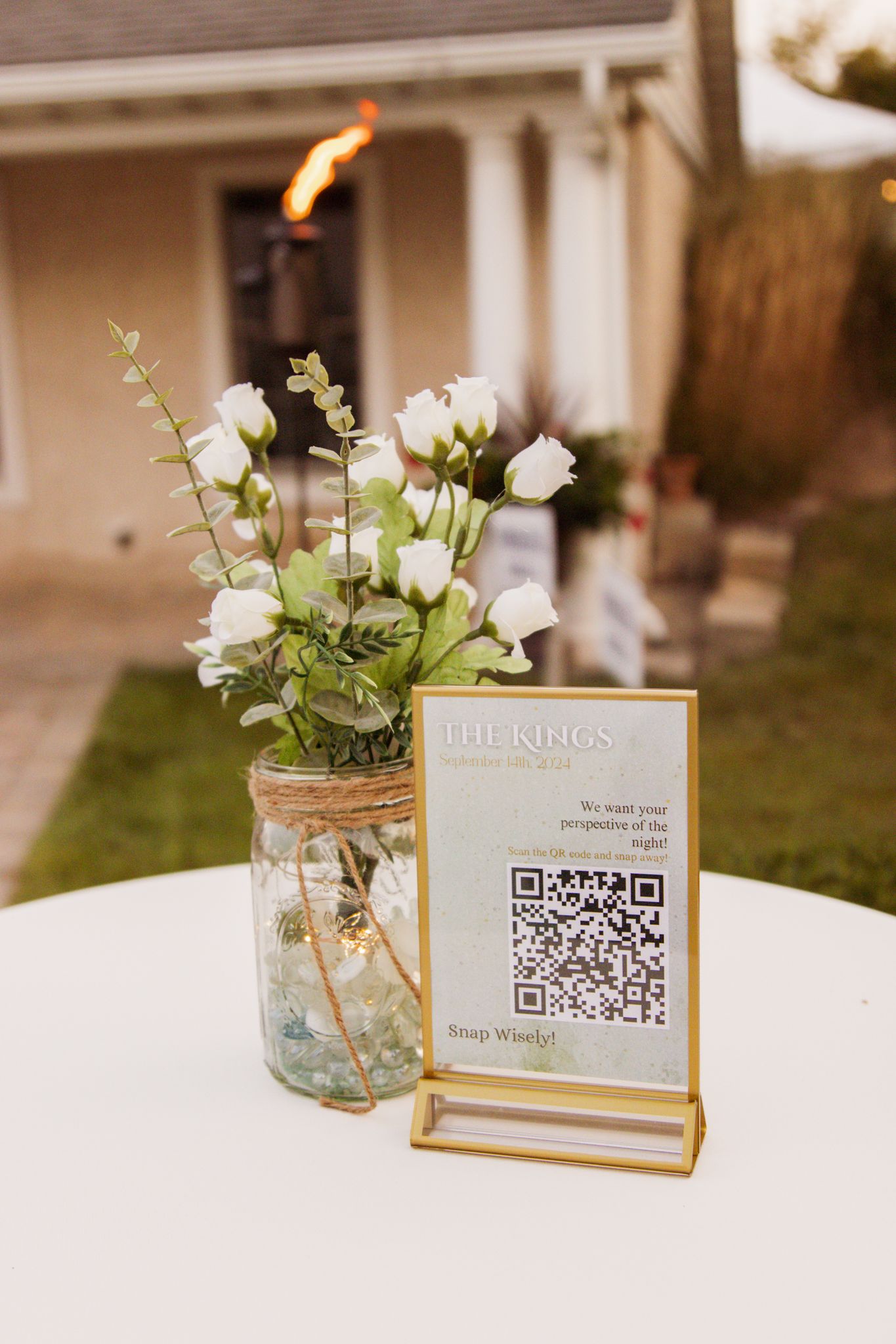 Elegant wedding reception table with white roses in mason jar and gold-framed QR code sign for The Kings wedding.