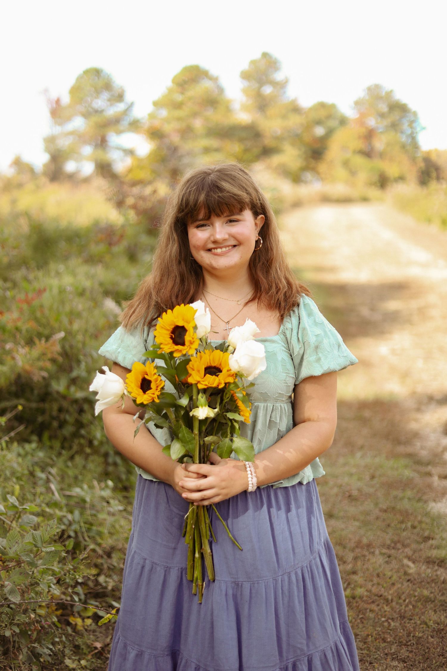 Person poses with sunflower bouquet on dirt path during golden hour.