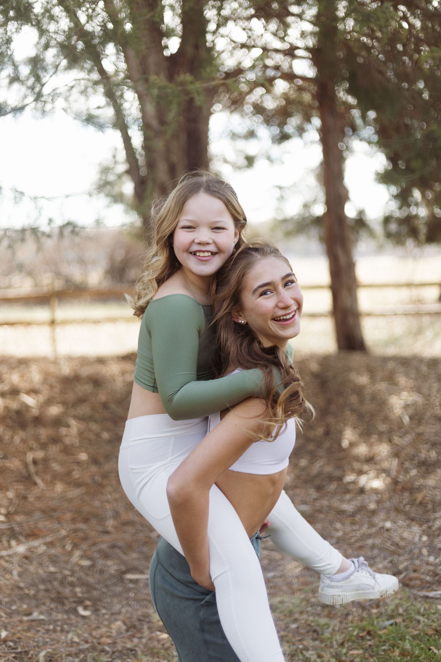 Two dancers share a playful piggyback moment outdoors among trees.