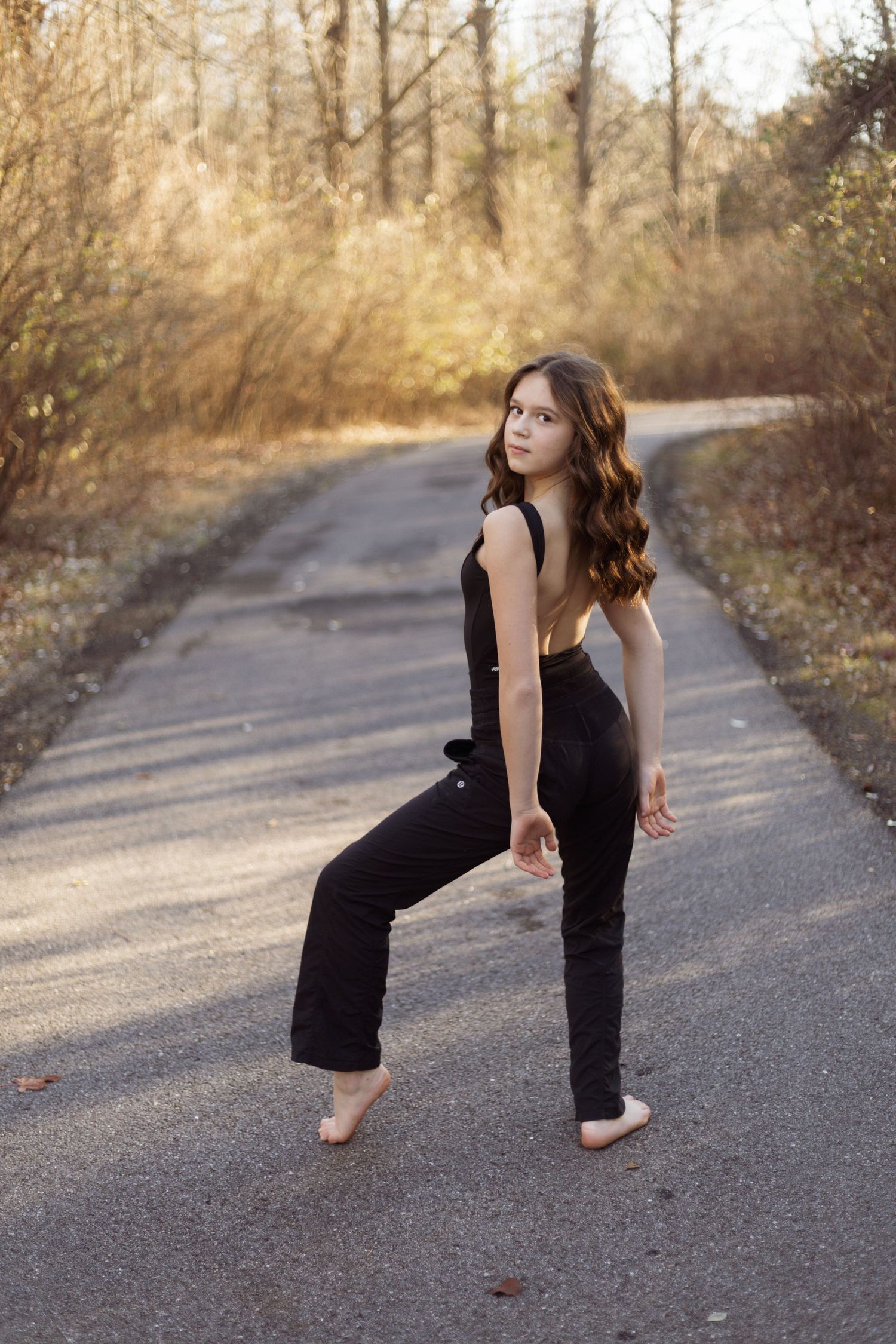 Dancer in black outfit poses on nature trail during golden hour.