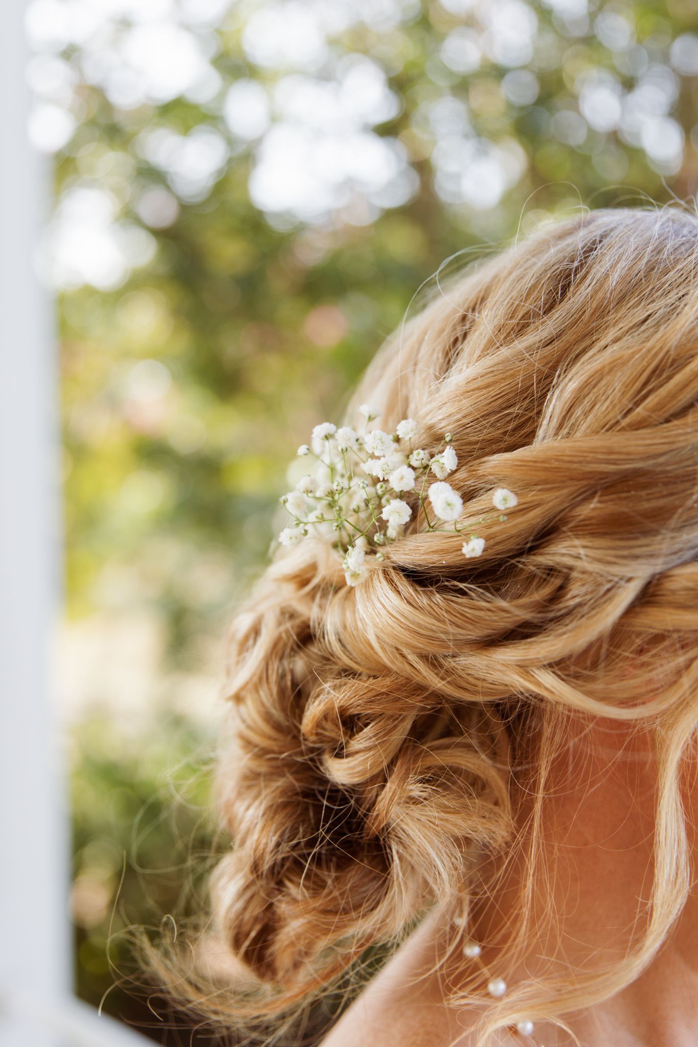 Elegant bridal updo with braided bun and delicate baby's breath flowers in blonde hair, perfect wedding hairstyle.