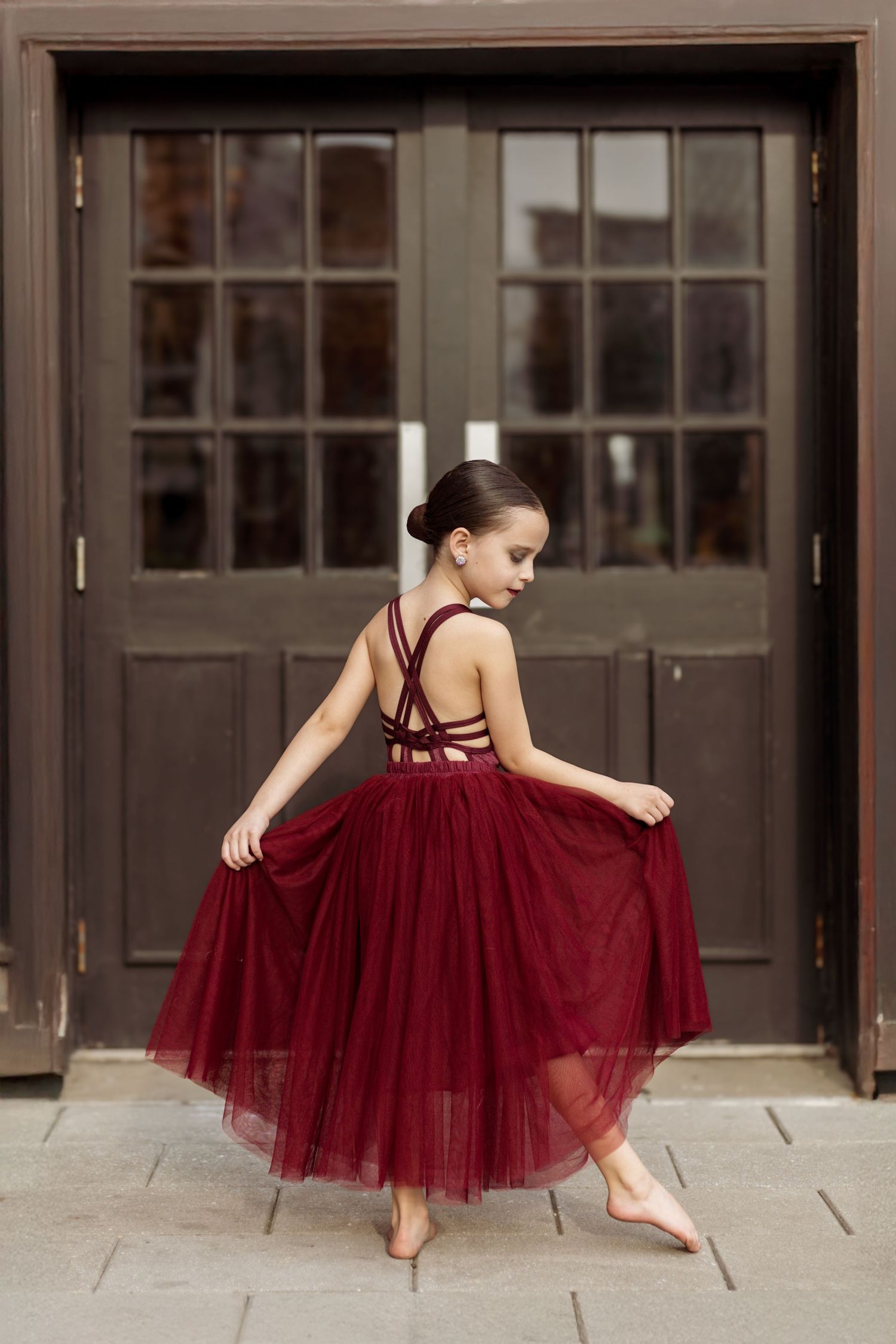 Dancer in burgundy dress poses elegantly in front of vintage double doors.