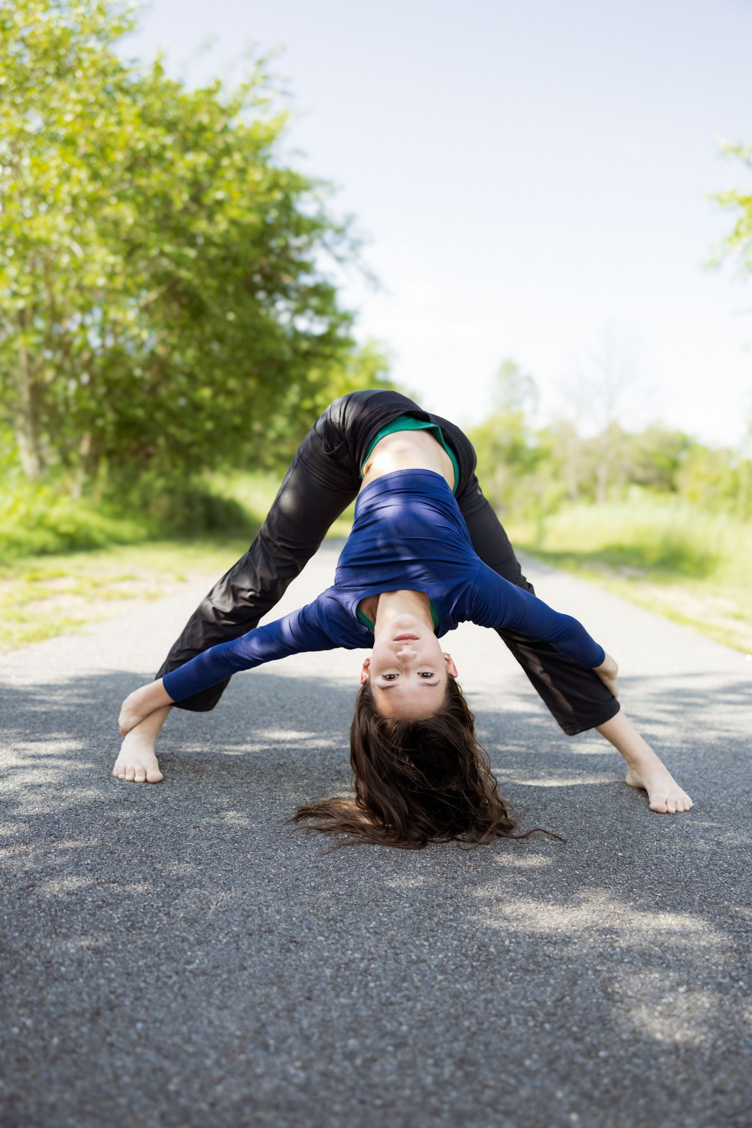A sequence of five photos shows a person laying on an asphalt road performing artistic movement poses outdoors.