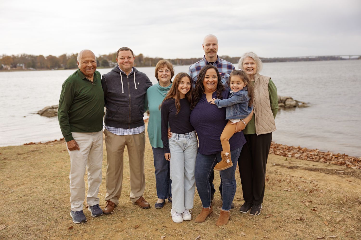 Multi-generational group poses together on a rocky shoreline during autumn.