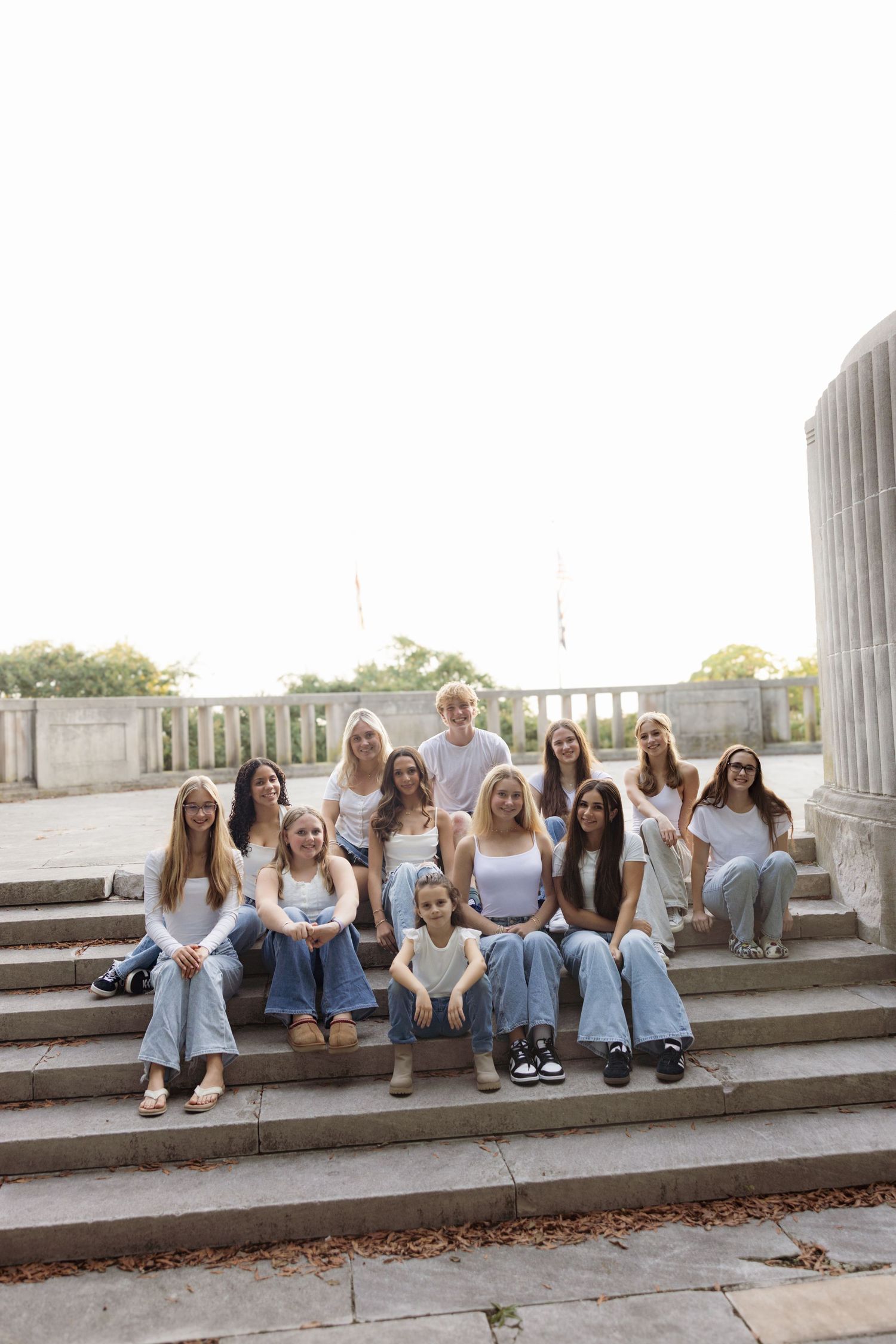 A group of friends sit together on outdoor concrete steps wearing casual denim and white outfits.