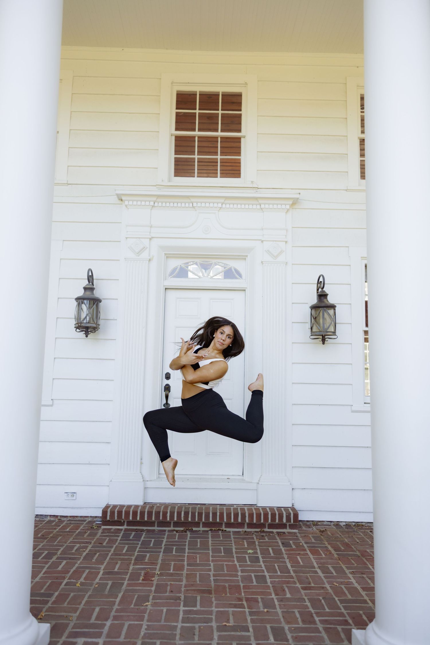 A dancer performs a graceful pose on a brick porch with white columns and walls.