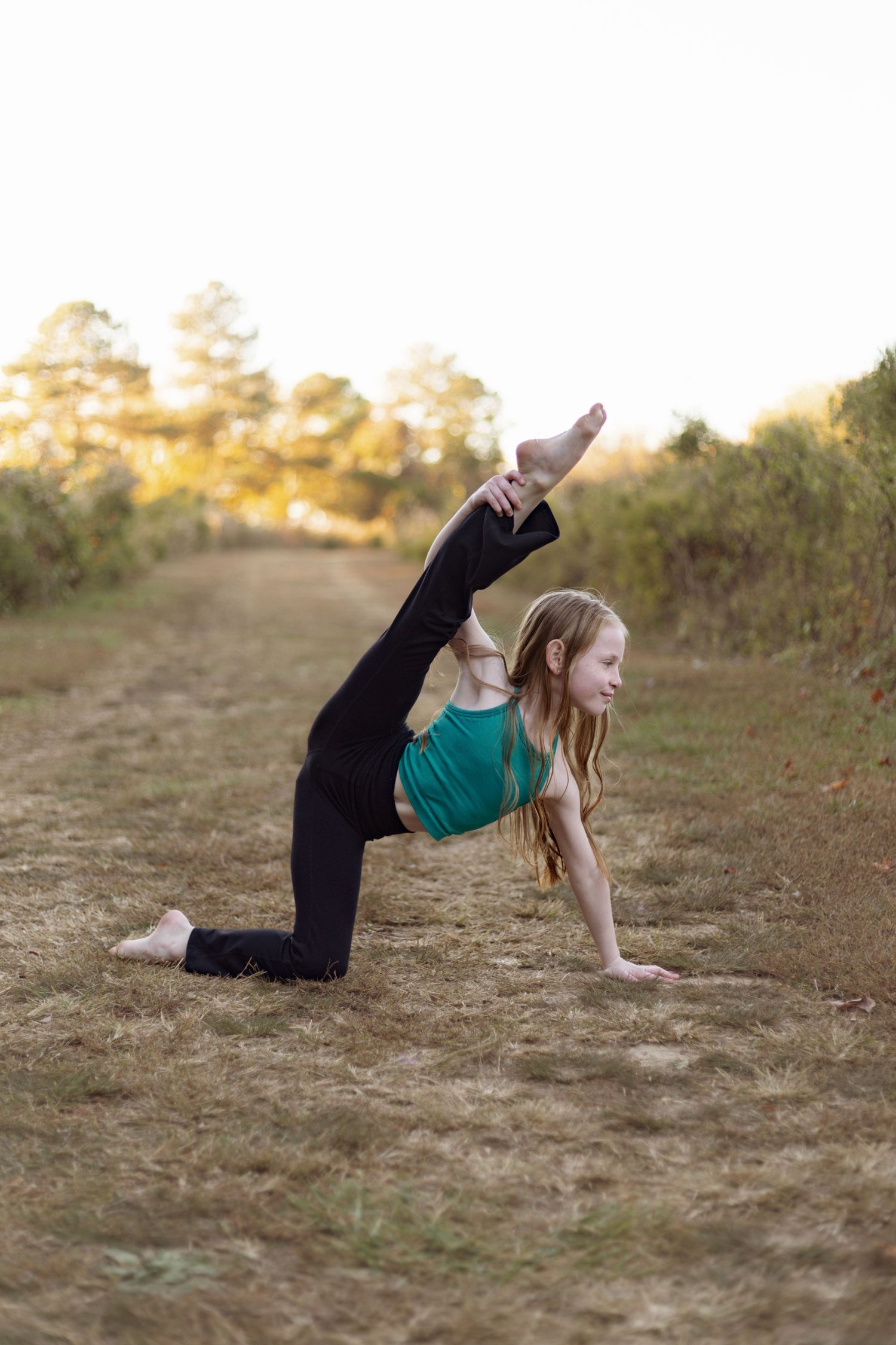 Dance pose performed on rustic dirt path with pine trees in background.
