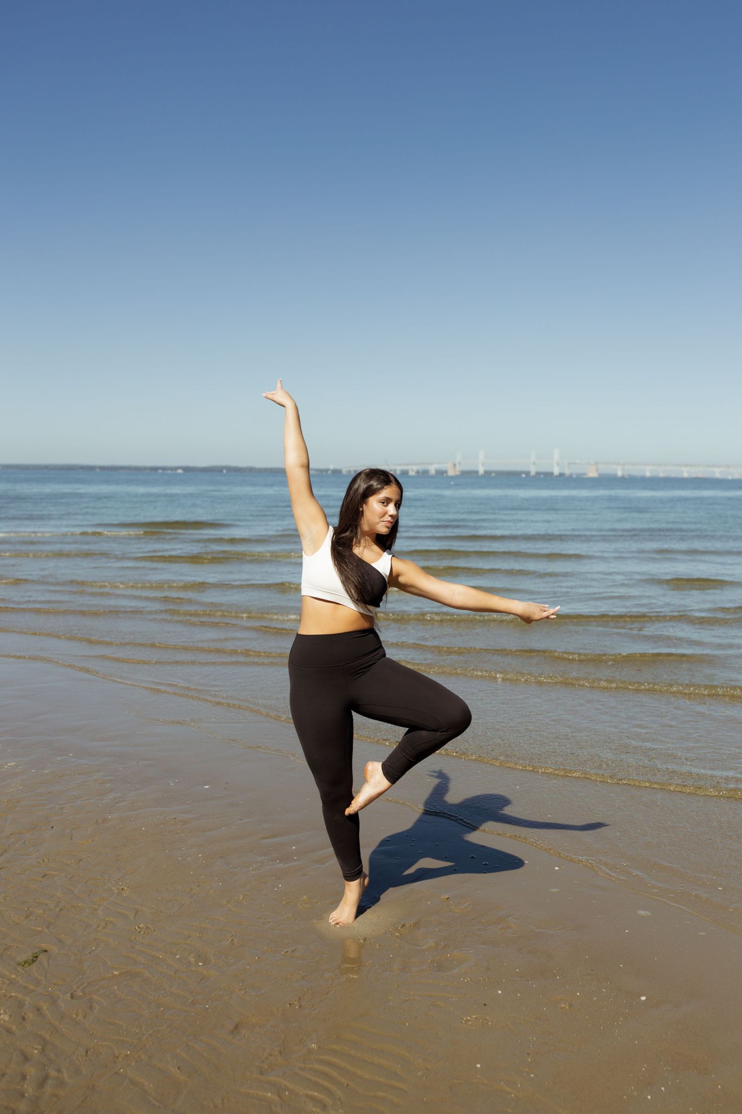 A person performs a graceful dance sequence on a sandy beach with the ocean and blue sky in the background.