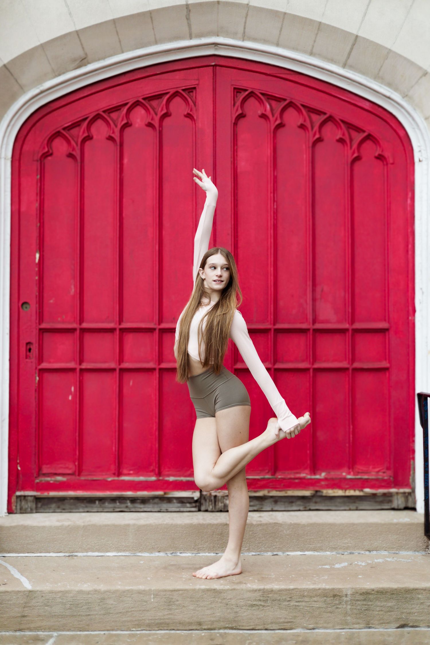 Dancer poses elegantly in front of ornate red gothic door.