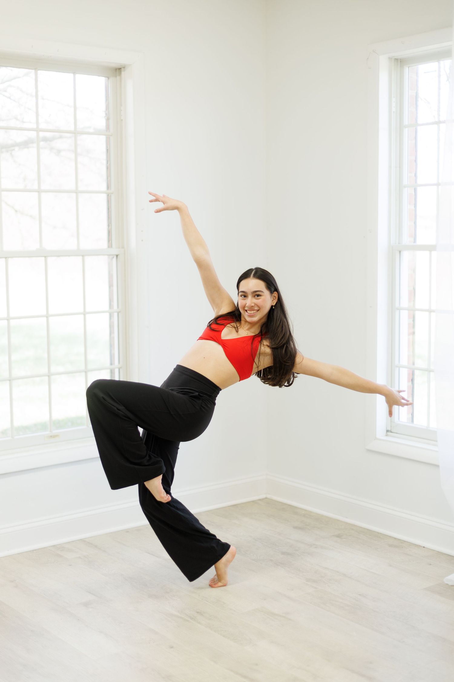 Dancer performs expressive movement in red crop top against white walls and windows.