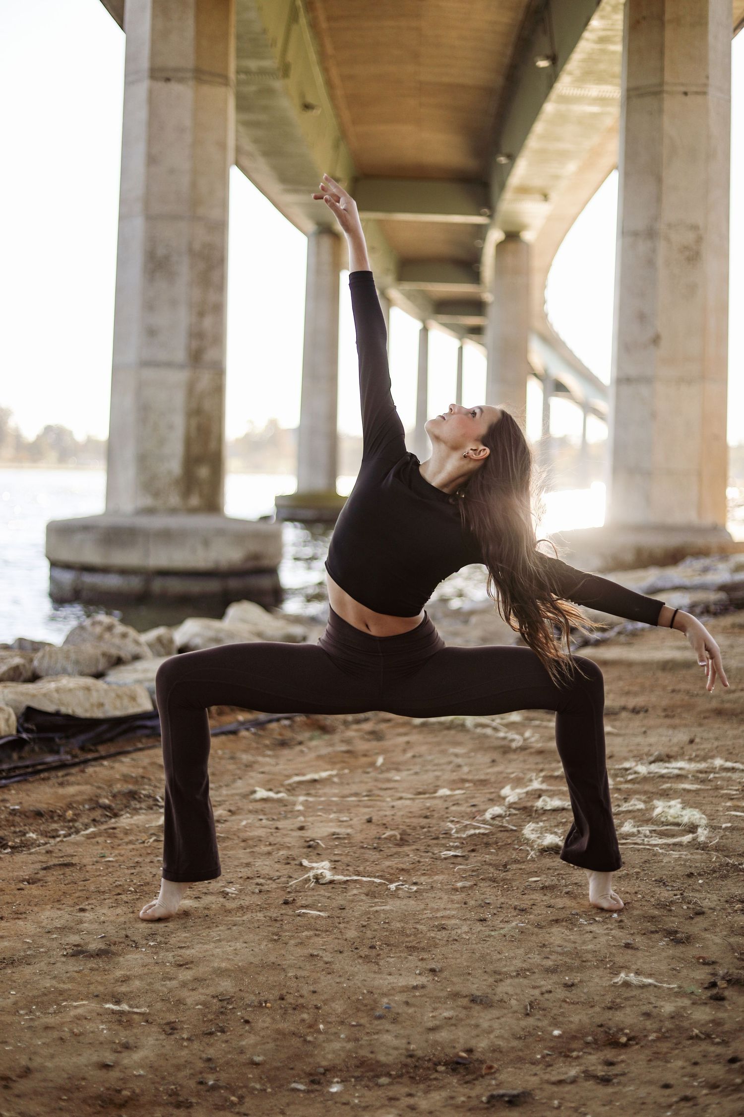 Dancer performs graceful pose under concrete bridge at sunset showing strength and flexibility.